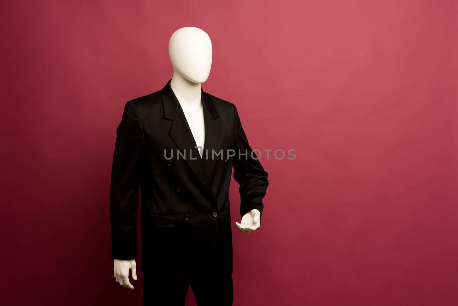 White male mannequin in a black business suit on a ruby background - image