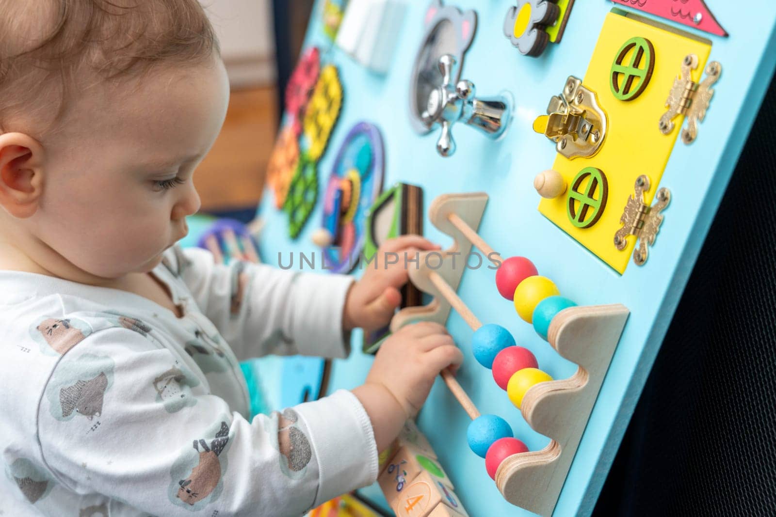 A baby moves round wooden elements on a busy board.