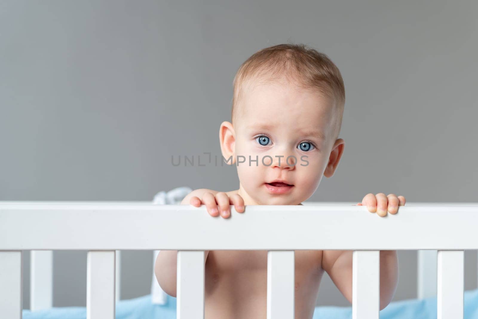 The baby is surprised and pulls himself up on the back of the crib with little effort.