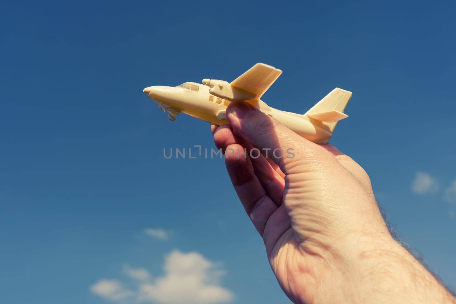 close up photo of male hand holding toy airplane against blue sky . image is retro filtered