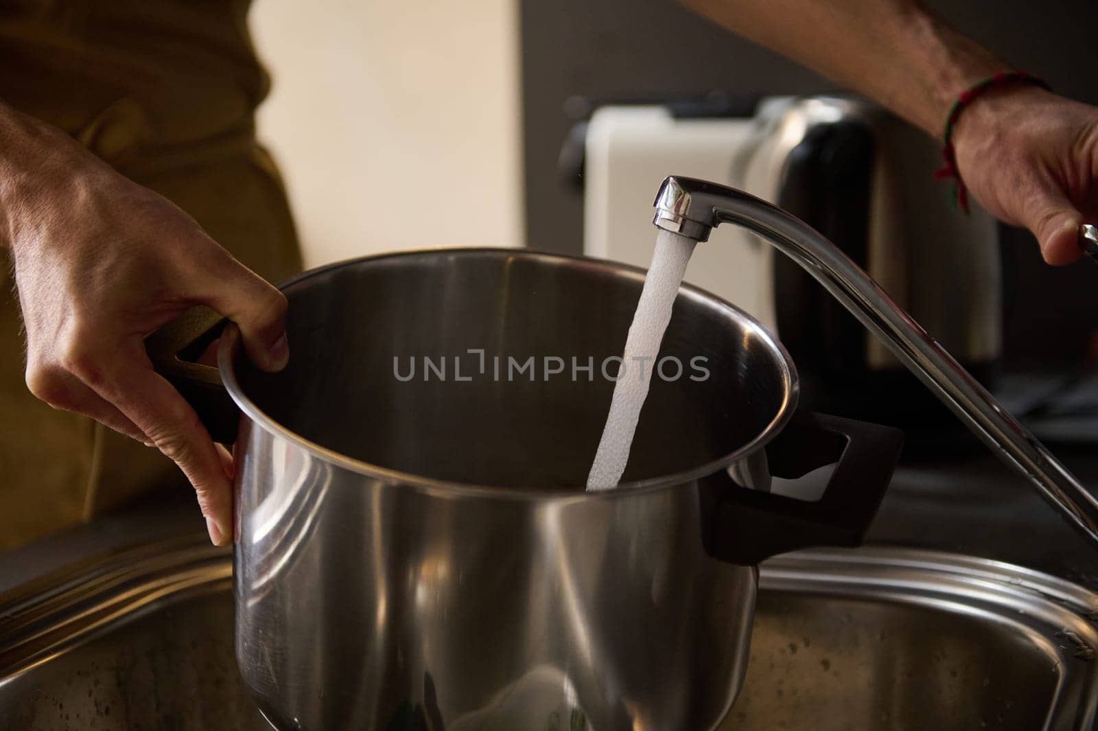 Man's hands filling a stainless steel saucepan with running water until it boils and cooks something. The concept of preparing food in the home kitchen. Close-up