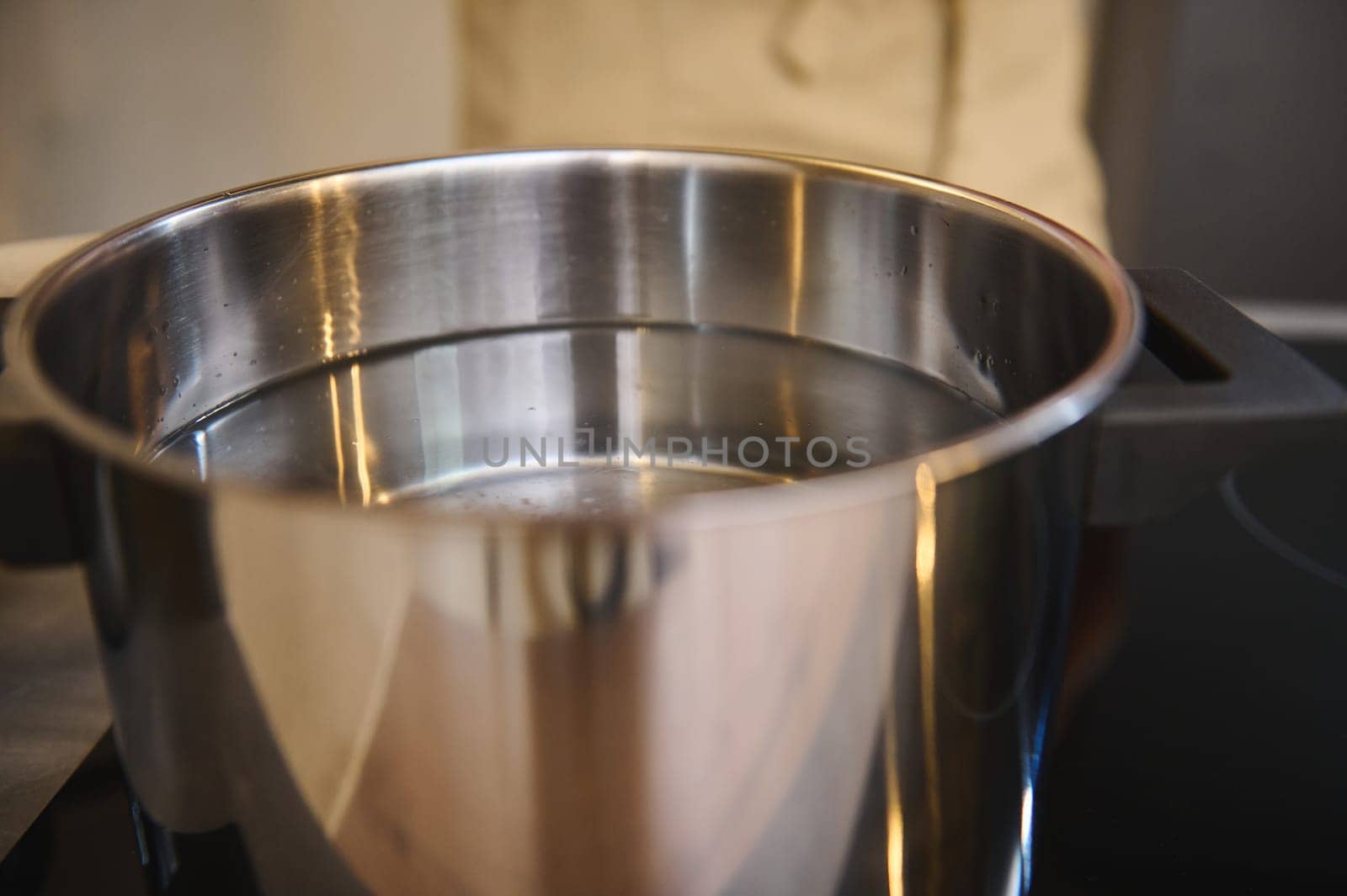 A stainless steel pan with water on an electric stove. Kitchen utensils. Chef boiling water for spaghetti on induction stove