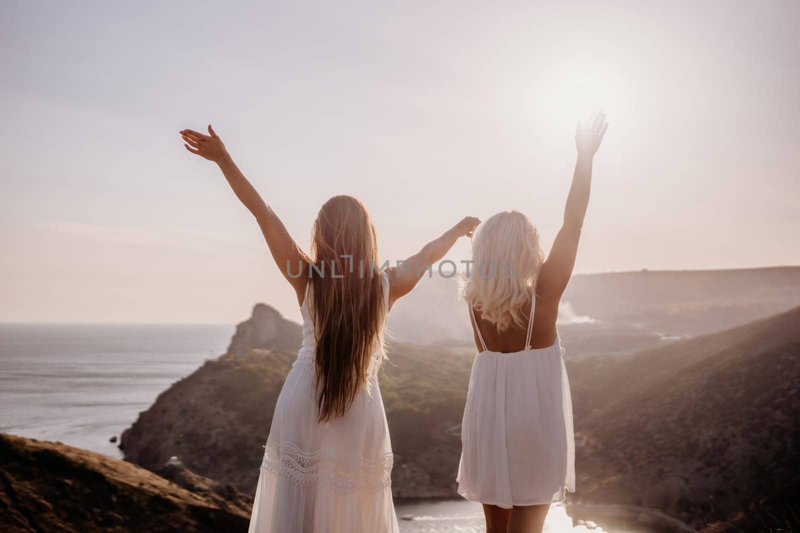 Two women are standing on a hill overlooking the ocean. They are holding hands and looking out at the water. The scene is peaceful and serene, with the sun shining brightly in the background