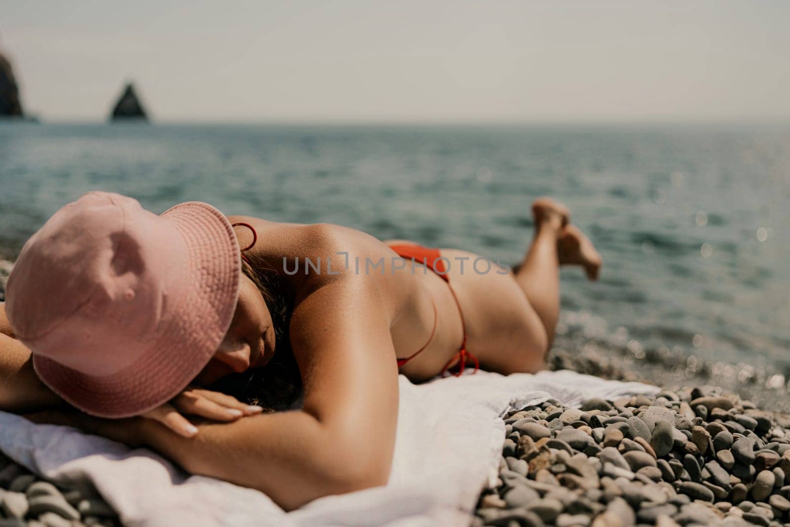 A woman sunbathes on the beach, lying on her stomach in a red swimsuit against the sea backdrop