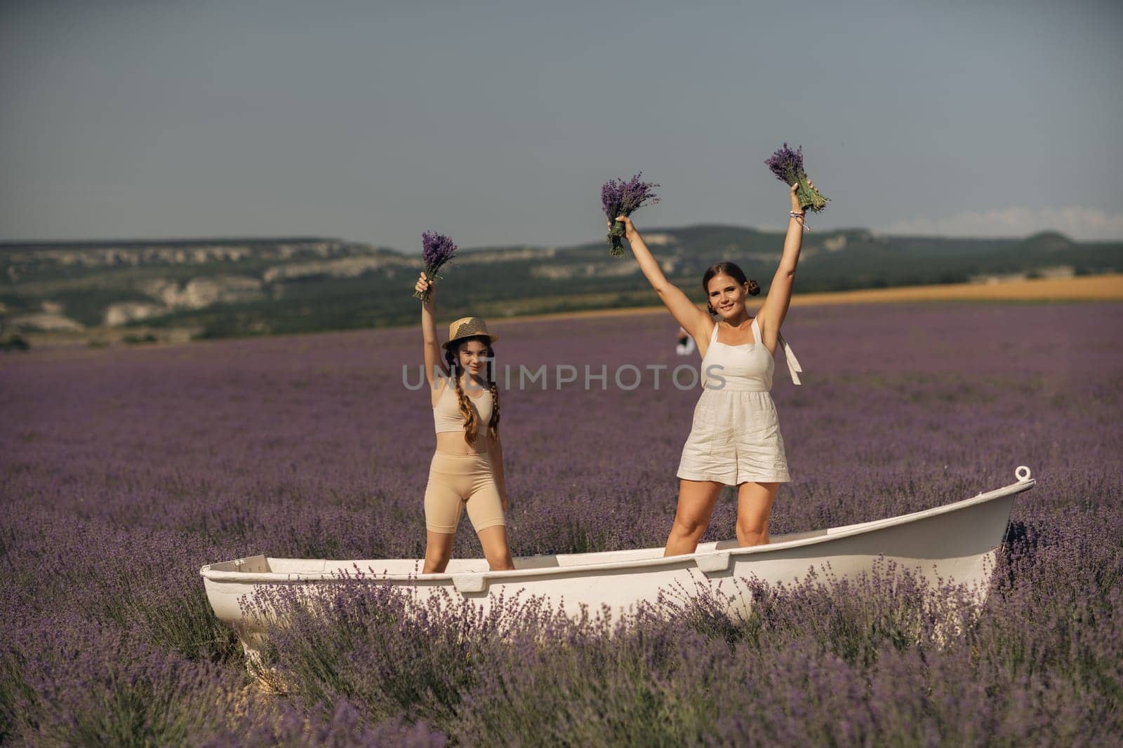 women and girl standing in a field of lavender, holding flowers and smiling. They are in a small boat, which is floating on lavender by Matiunina