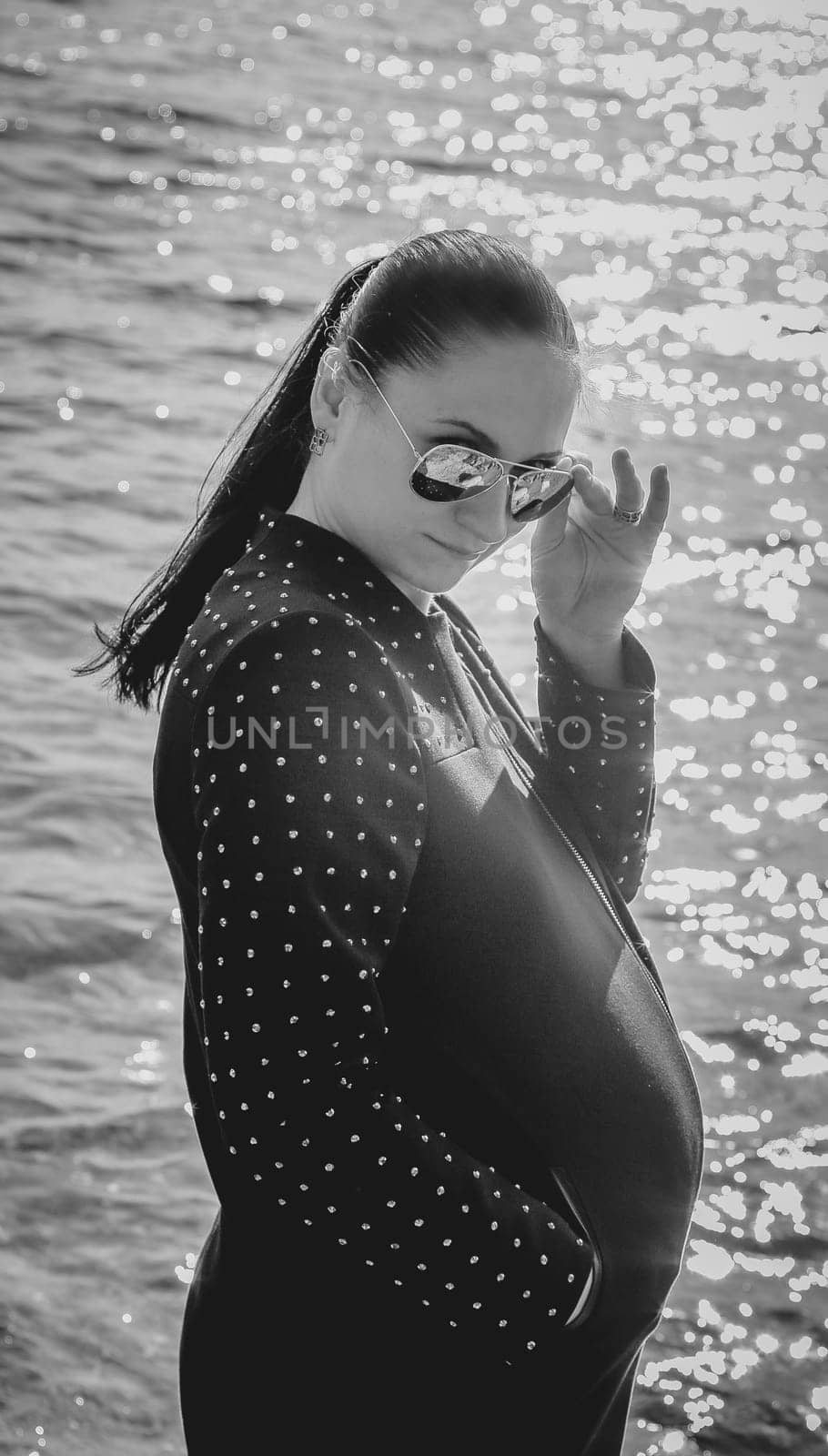Monochrome photo of a pregnant brunette girl in sunglasses against the background of the sea