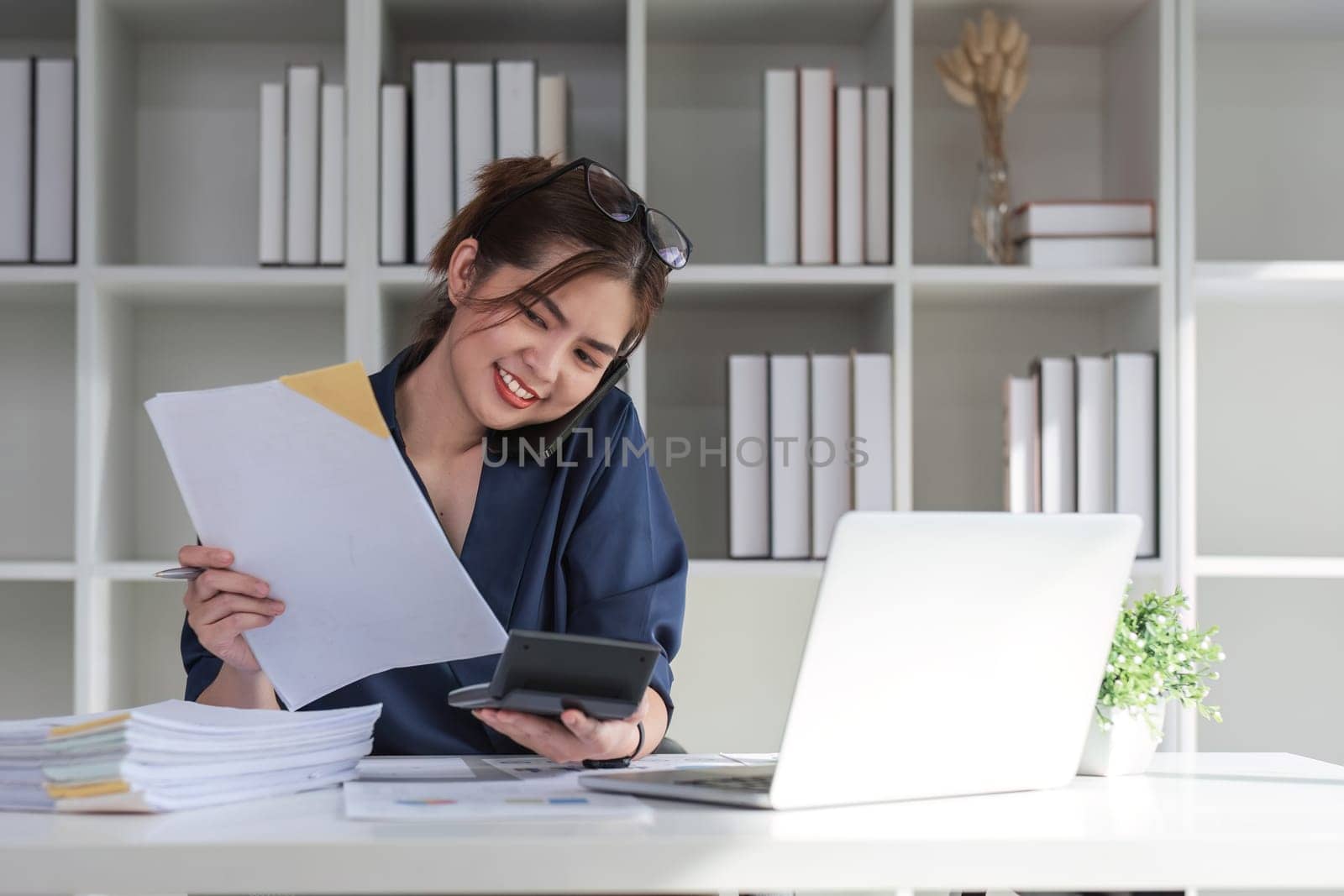 Young businesswoman using the phone talking working on starting a business and calculating finances with a calculator. by wichayada