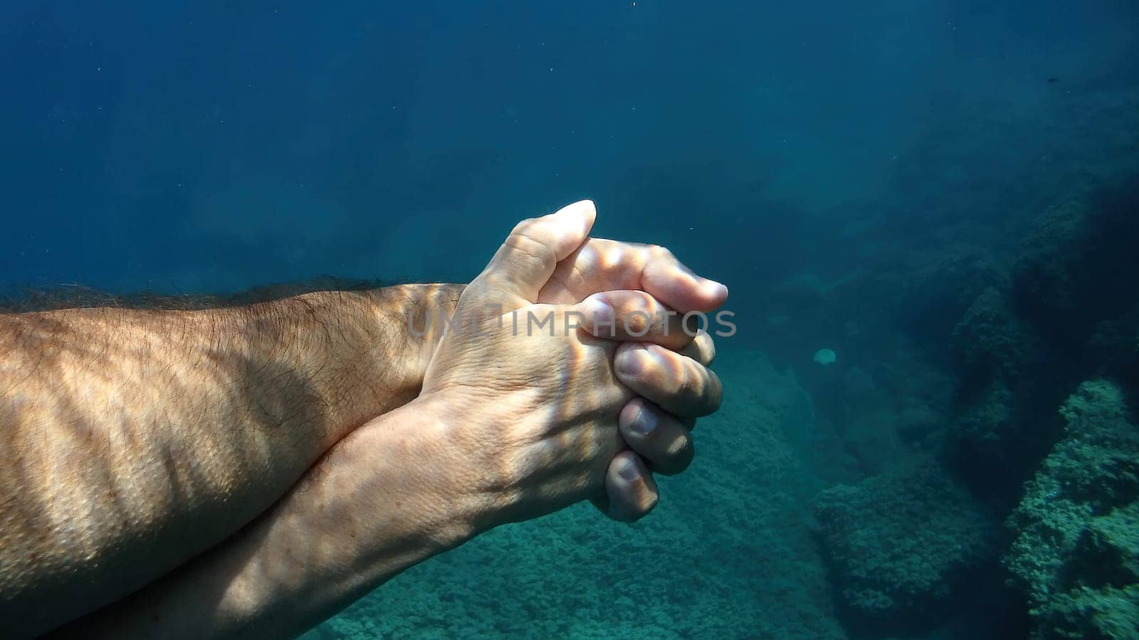 man and woman crossed human hands underwater detail by AndreaIzzotti