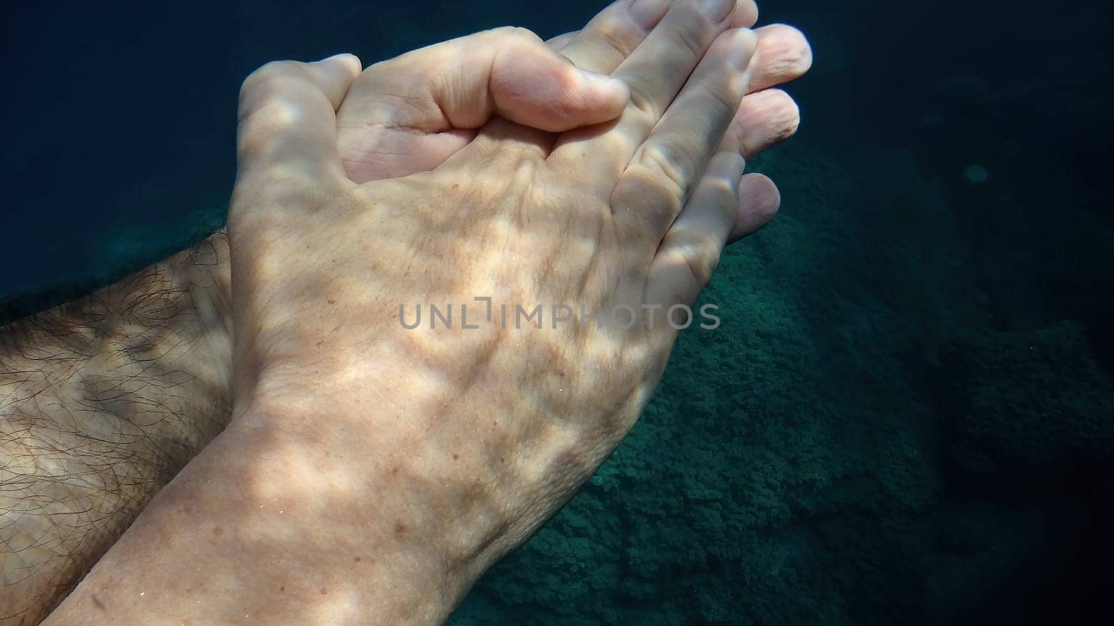 man and woman crossed human hands underwater detail by AndreaIzzotti