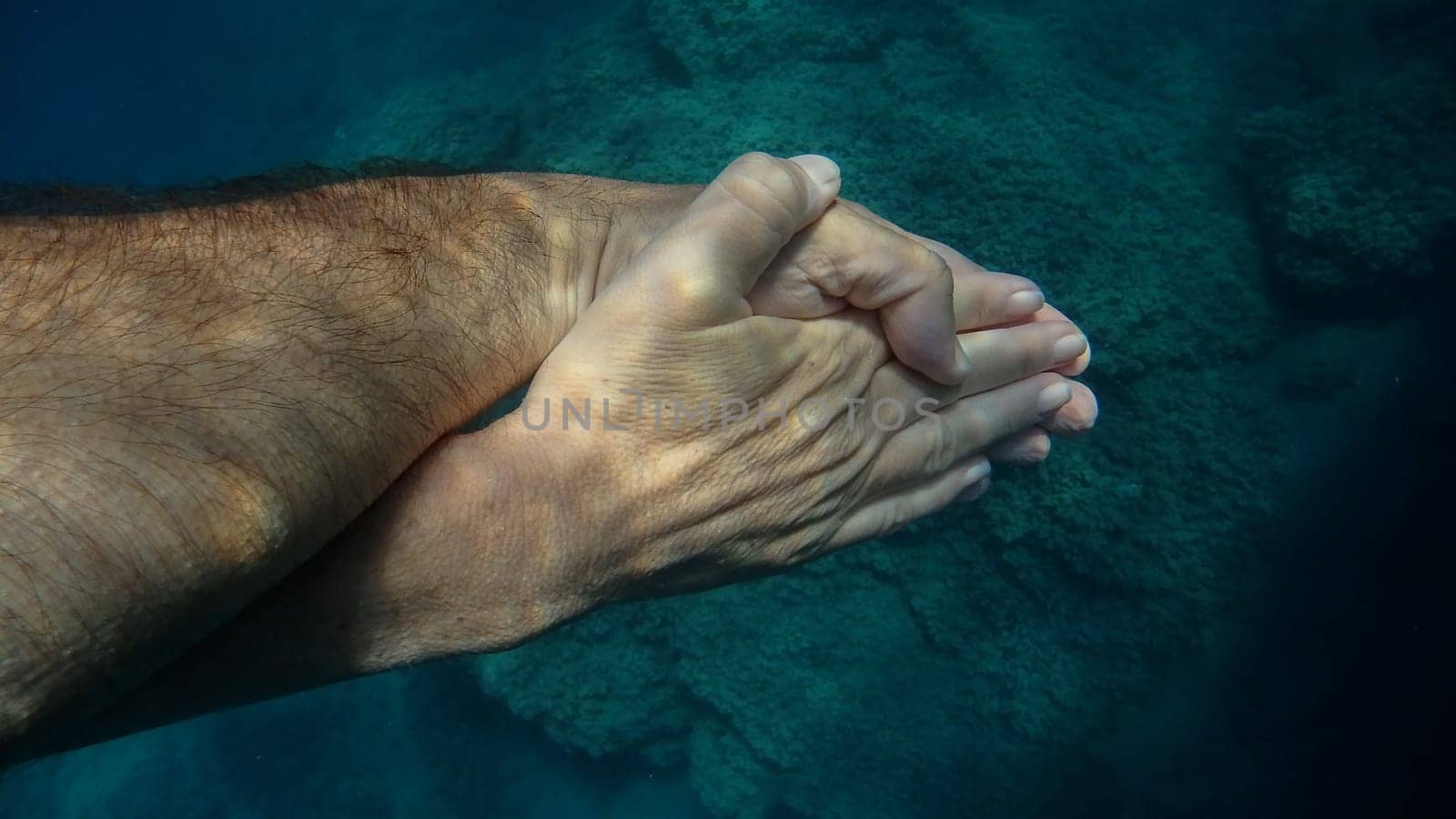 man and woman crossed human hands underwater detail by AndreaIzzotti