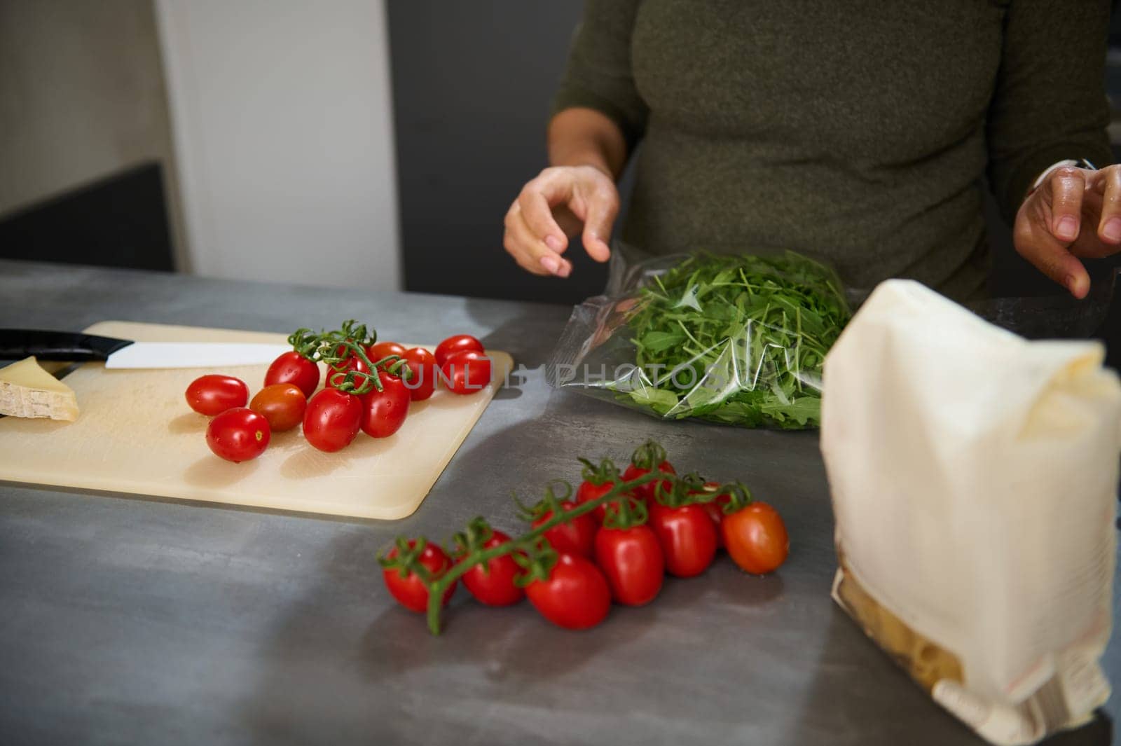 Fresh bunch of tomato cherry, arugula leaves and raw Italian pasta in paper packet on the kitchen table. Healthy eating, culinary, diet concept. Copy space for advertising text