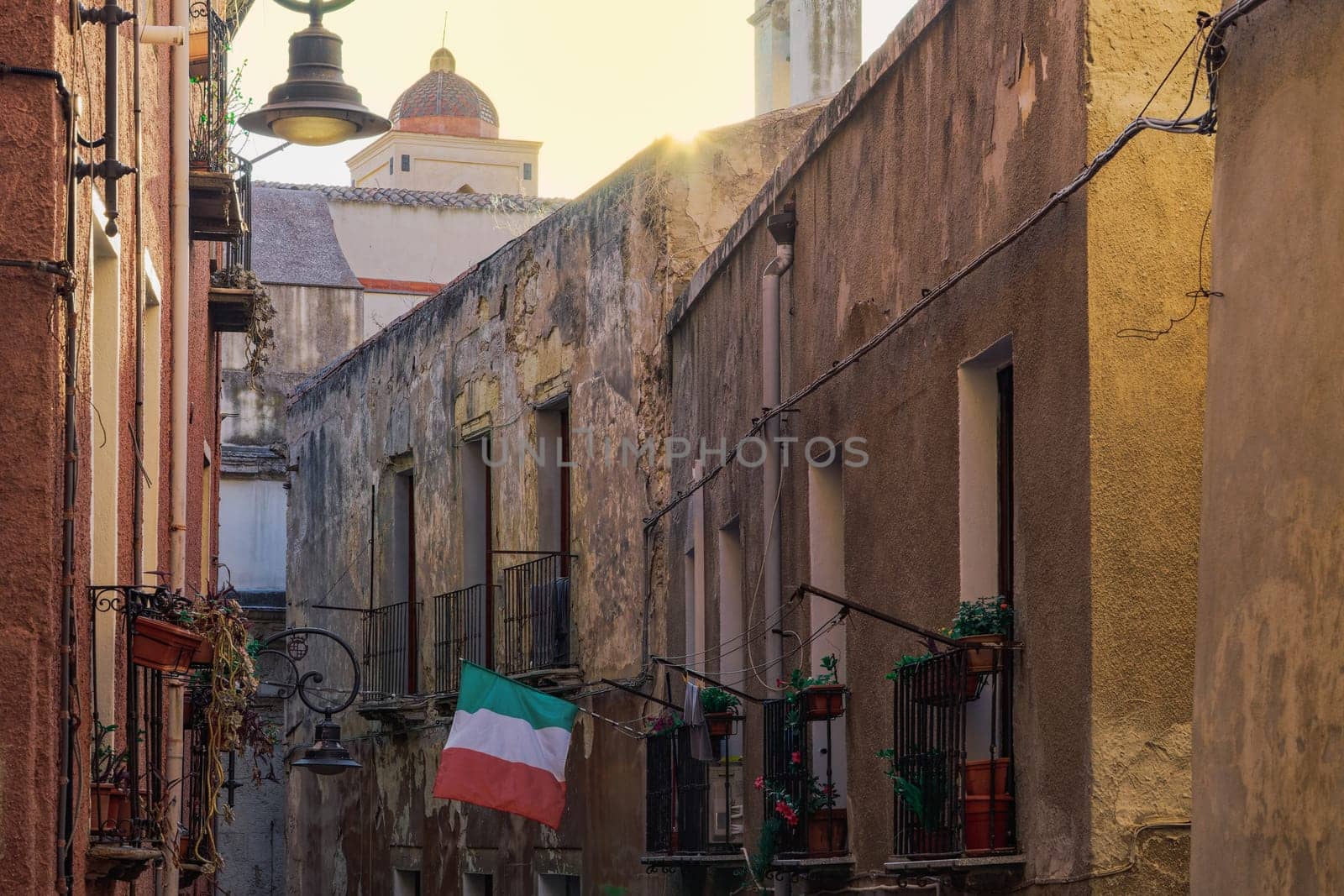 Cagliari citadel alley with traditional buildings with iron balconies and Italian flag waving in Sardinia Island, Italy.
