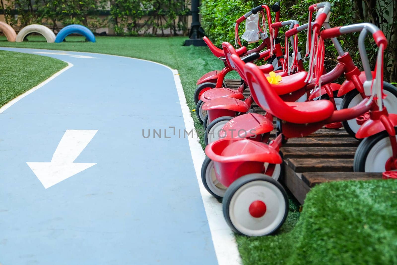 Red tricycles line up beside a track in a children's playground area by ponsulak