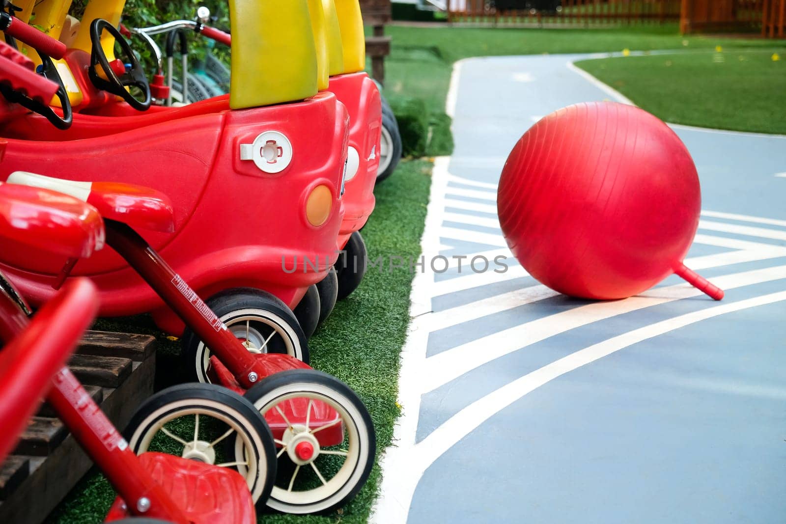 Colorful playground equipment with red toy cars and a ball on artificial turf