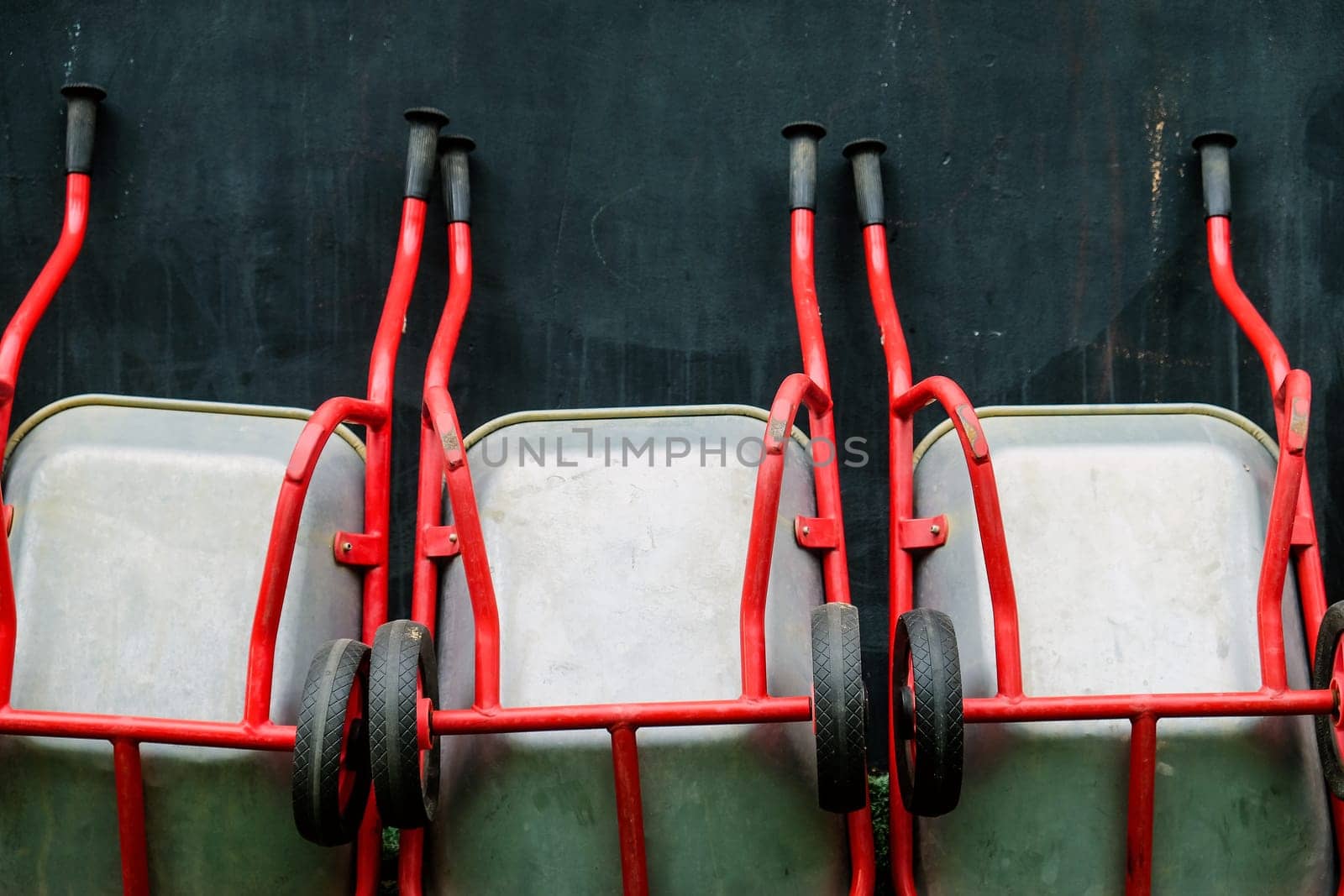 Array of red wheelbarrows lined up against a dark textured wall