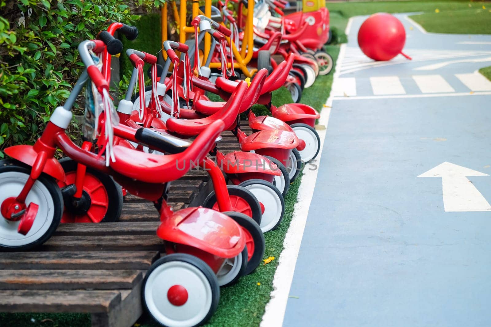 Red tricycles line up beside a track in a children's playground area by ponsulak