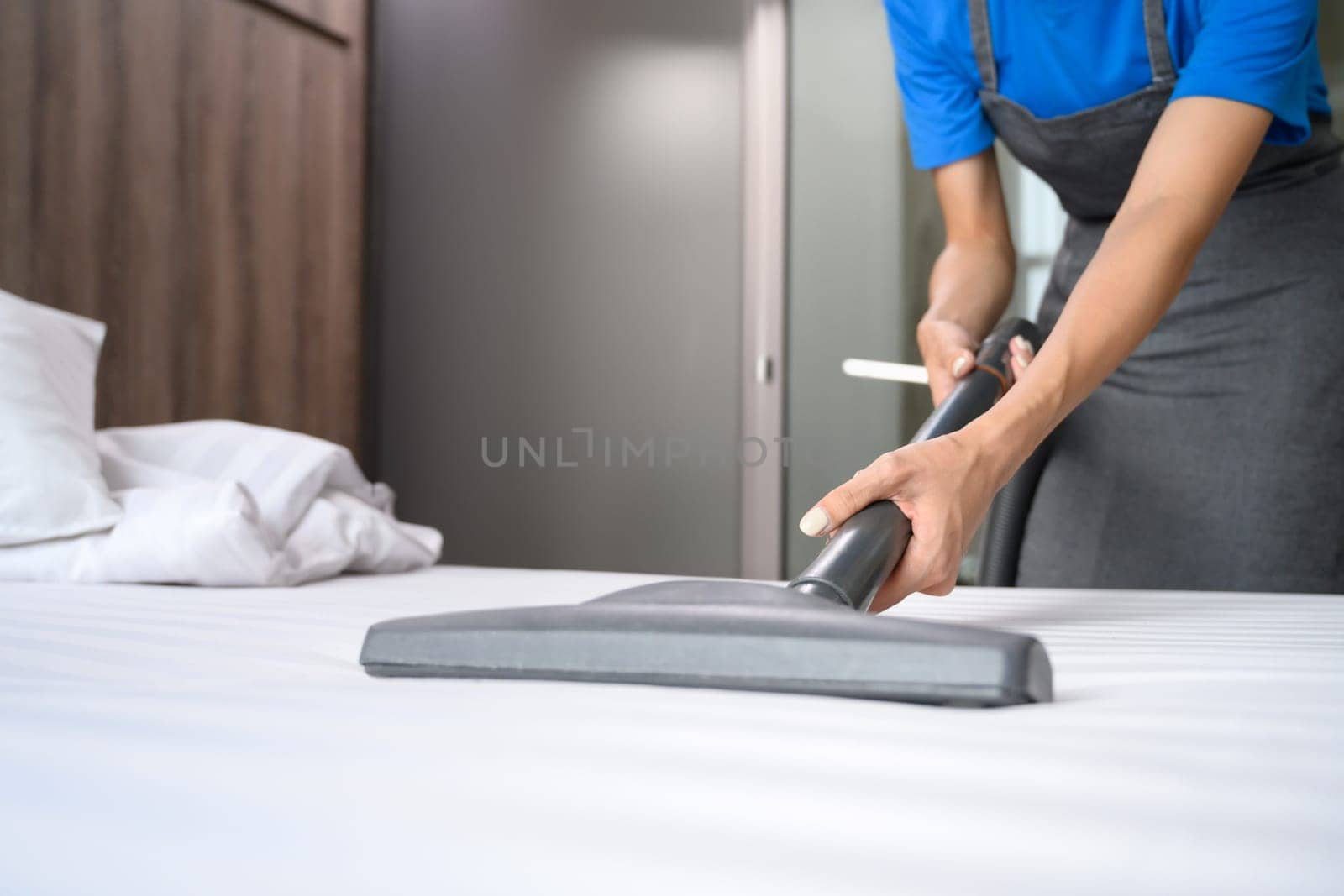 Female housekeeper removing dust and dirty on mattress with vacuum cleaner. Cleaning service concept.