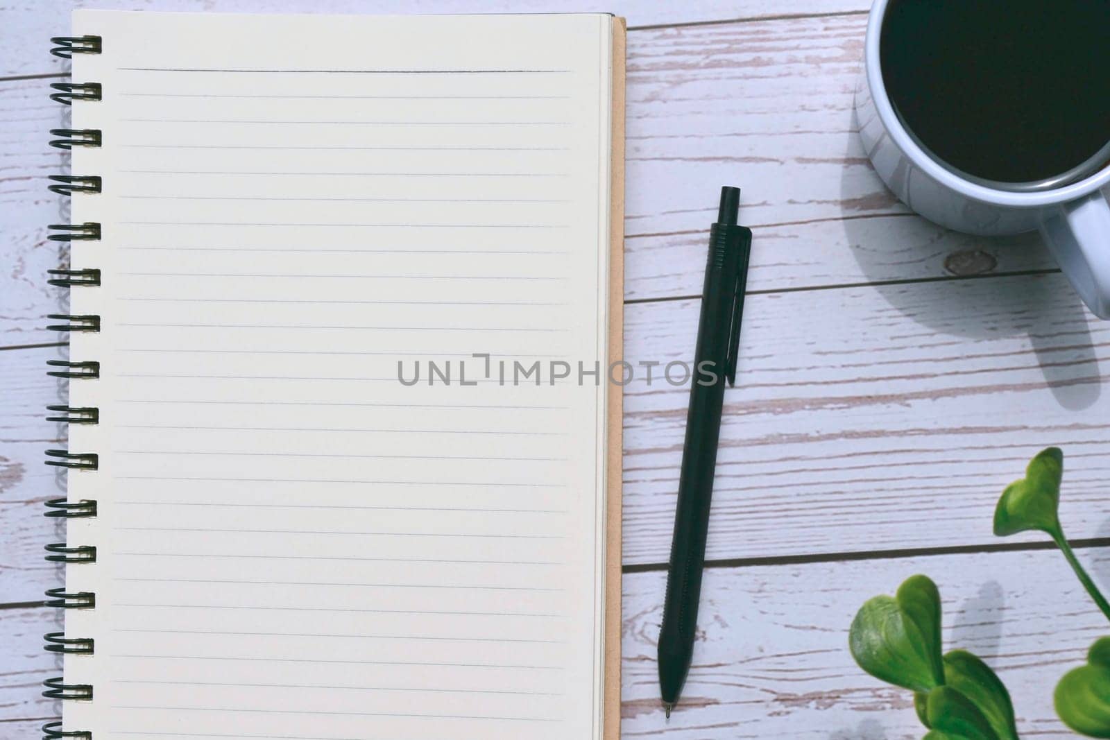 Top view of notepad and pen with cup of coffee on wooden desk. Copy space.