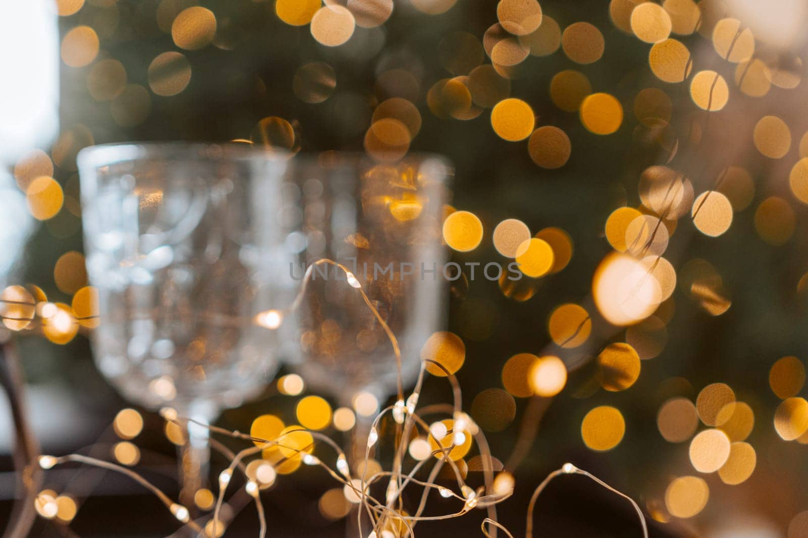 Champagne glasses, New Year decor. New Year's festive setting, family holidays.Two glasses of champagne are on the table against the background of New Year's decorated tree. by Matiunina