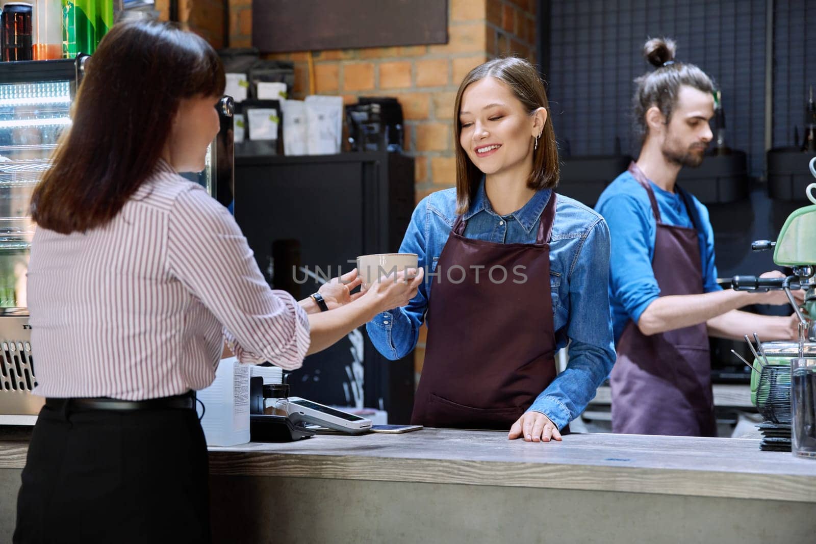 Woman customer of coffee shop near counter with cup of coffee talking to restaurant workers by VH-studio