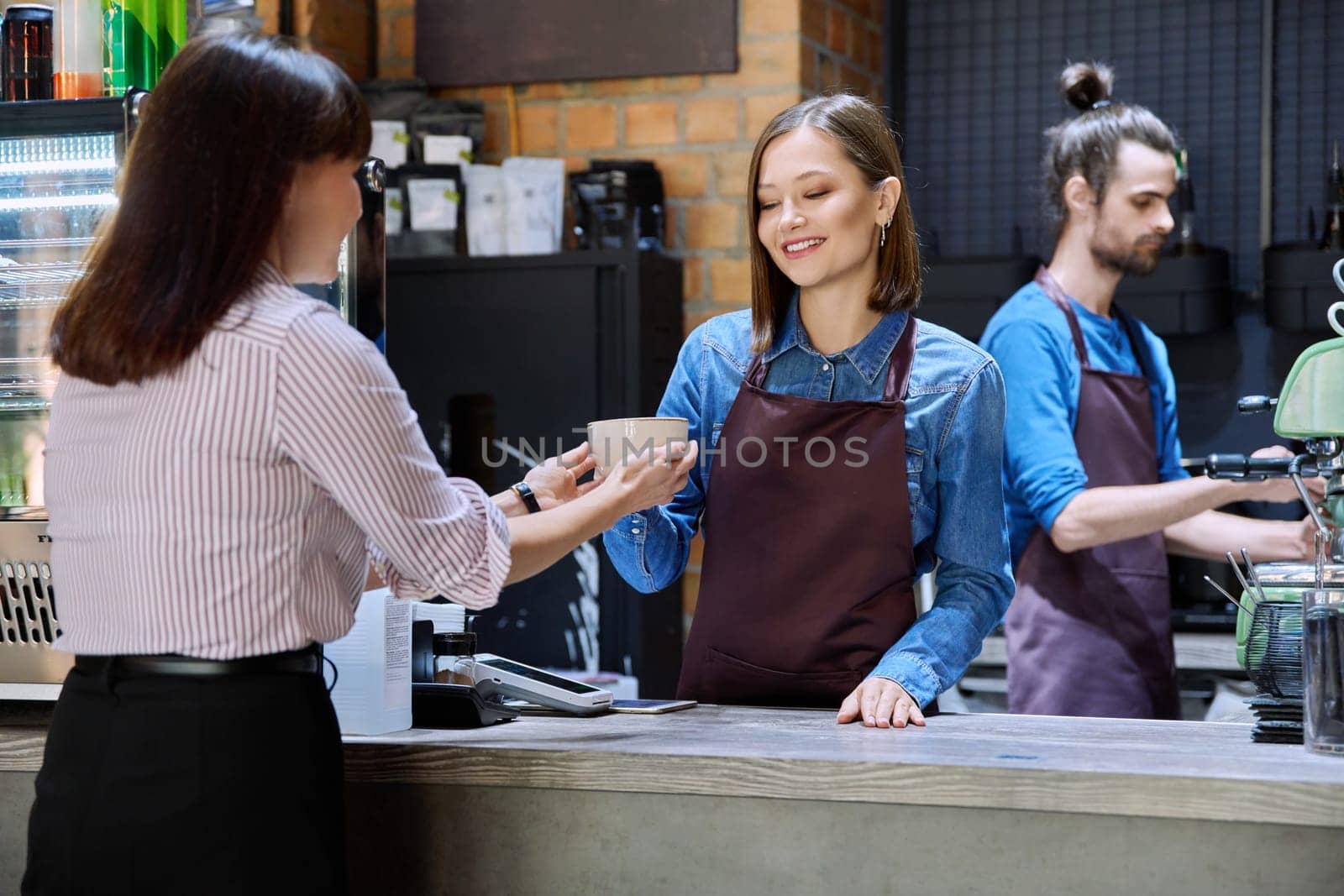 Woman customer of coffee shop near counter with cup of coffee talking to restaurant workers owners. Workplace at bar, colleagues, partners in food service, work, entrepreneurship, small business