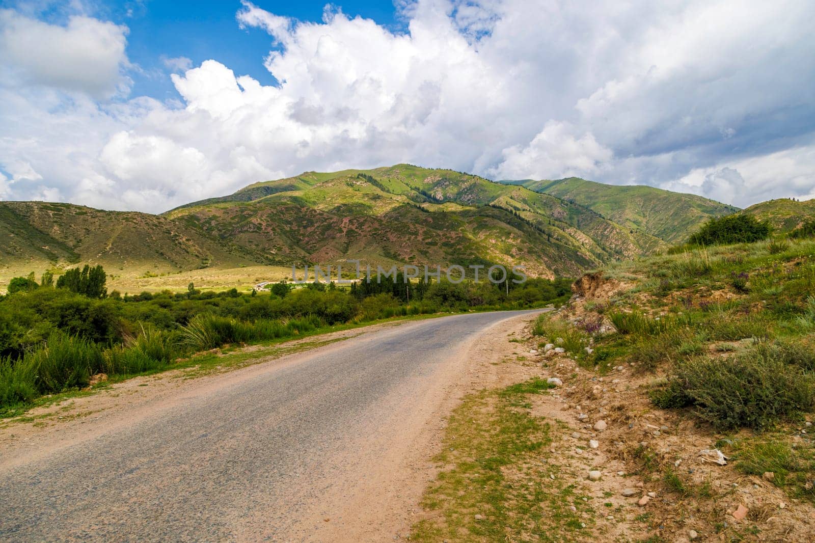 country road with mountains, grass, and clouds in the background by z1b