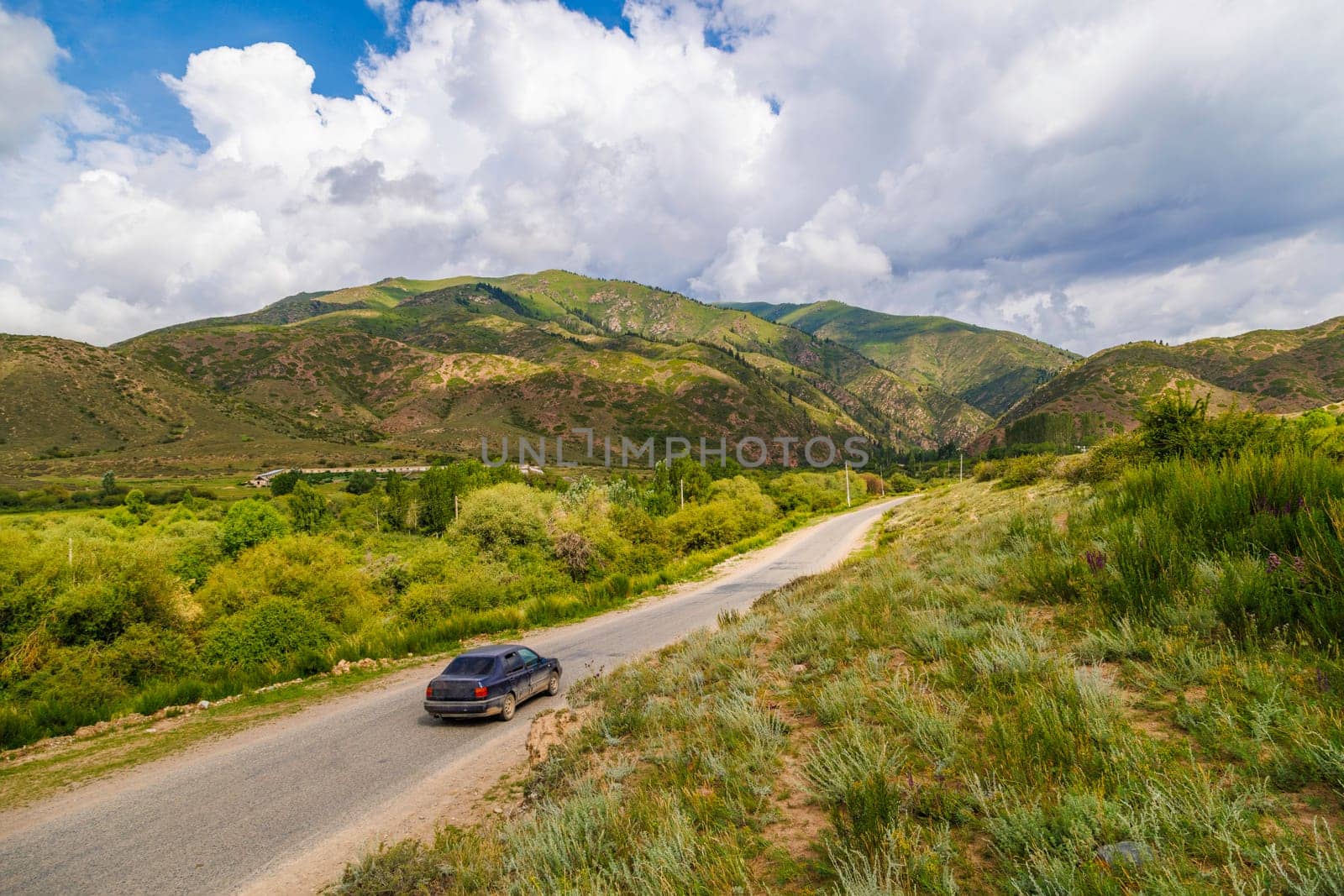 Car driving on country road with mountains, grass, and clouds in the background by z1b