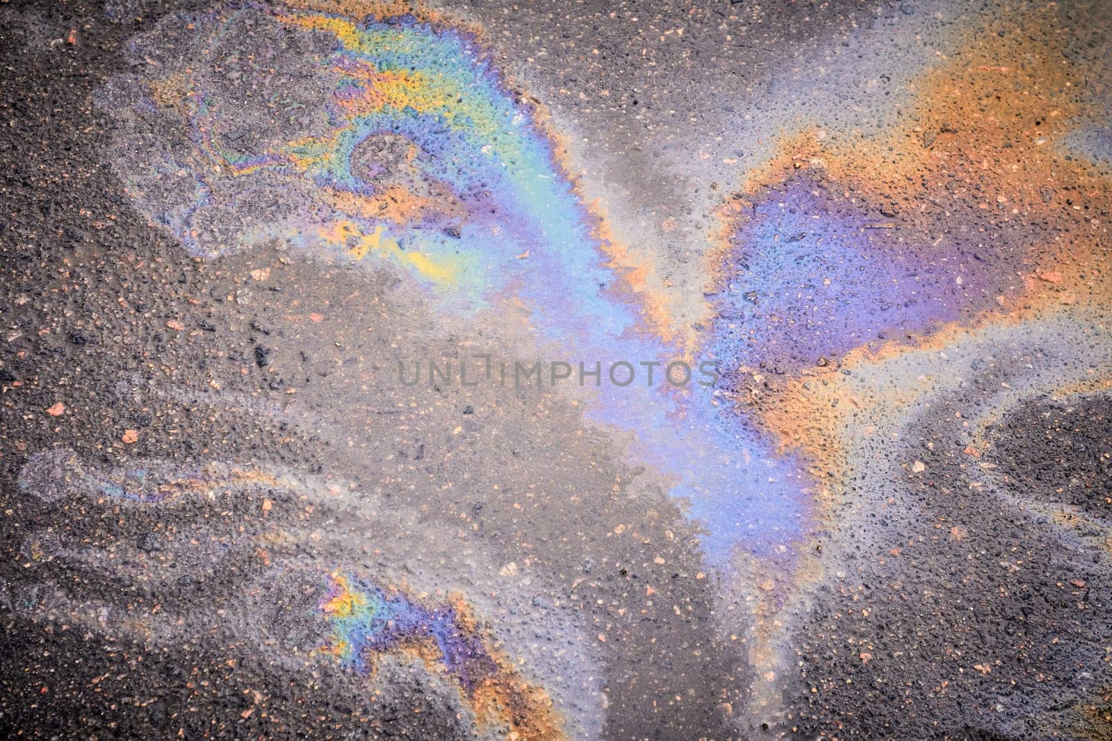 Leakage of oil or gasoline from under the car on the asphalt in the parking lot. Oil slick on the asphalt road background by AliaksandrFilimonau