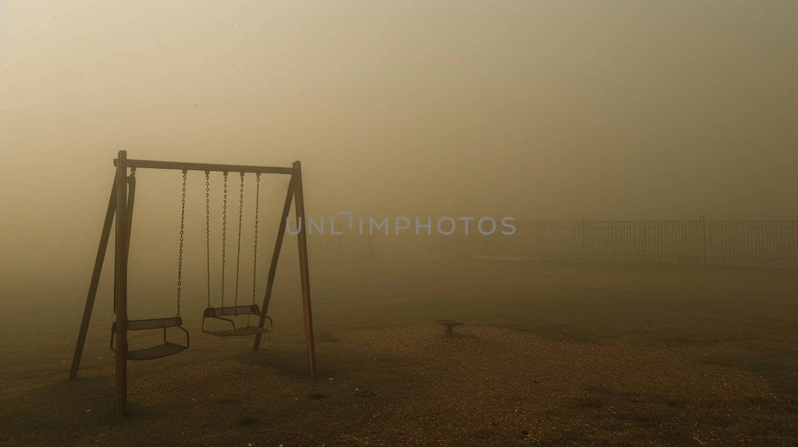 A haunting image of a playground overtaken by intense smog, where swings stand empty, evoking unease and isolation