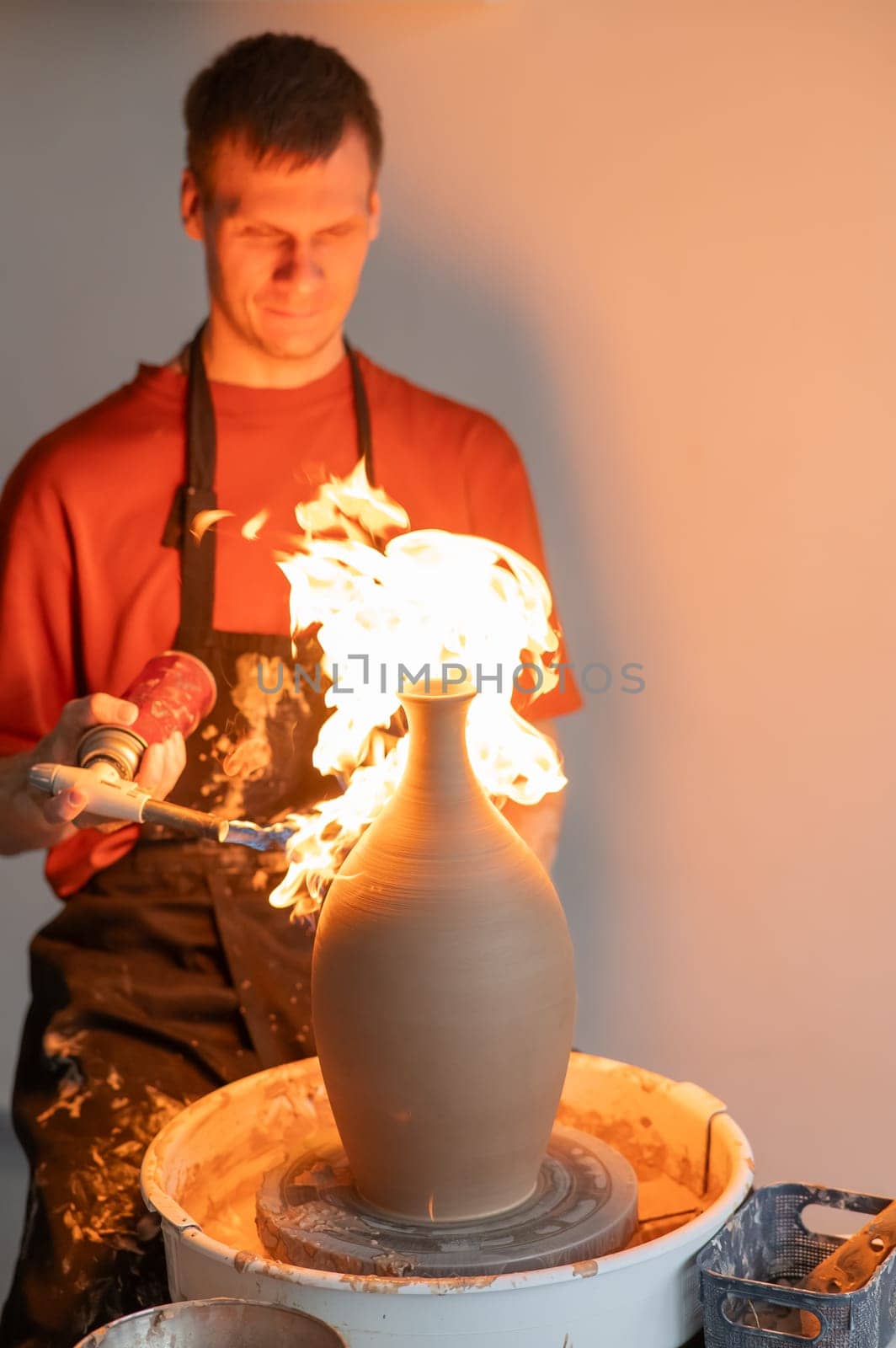 A potter burns a jug with a gas burner on a potter's wheel. Vertical photo