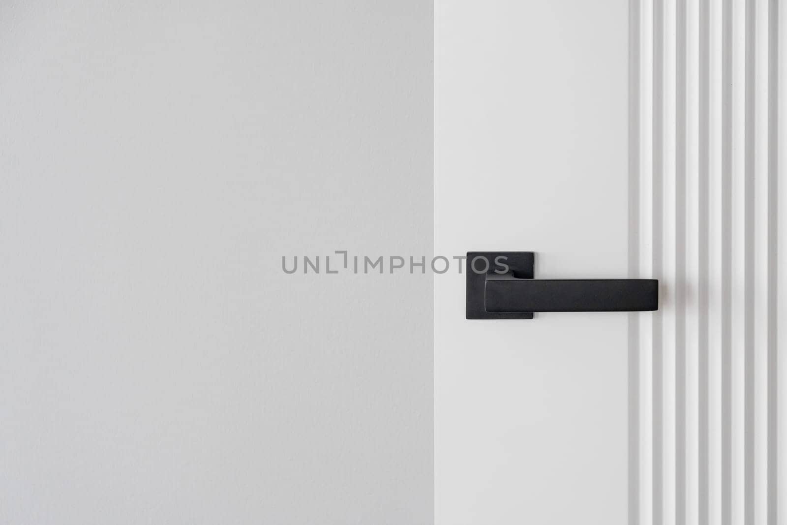 Modern black door handle on white wooden door in interior. Knob close-up elements. Door handle, fittings for interior design. Element of interior design