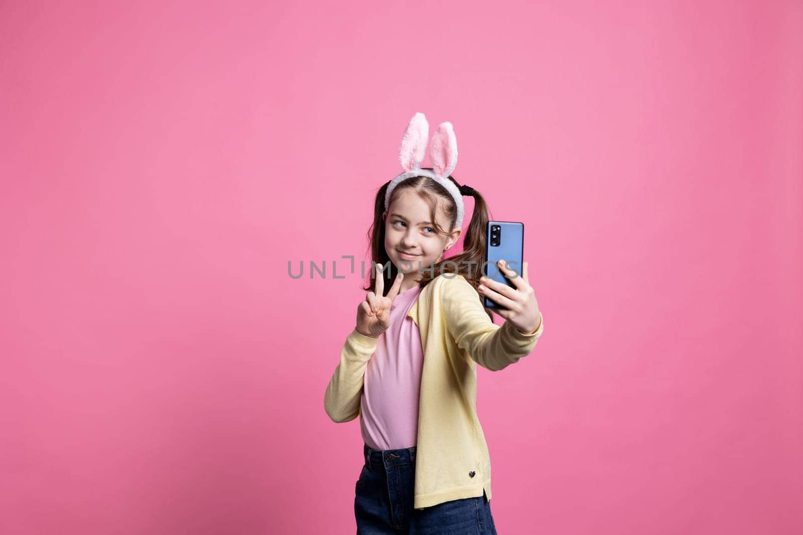 Joyful happy child taking pictures and showing peace sign on phone by DCStudio