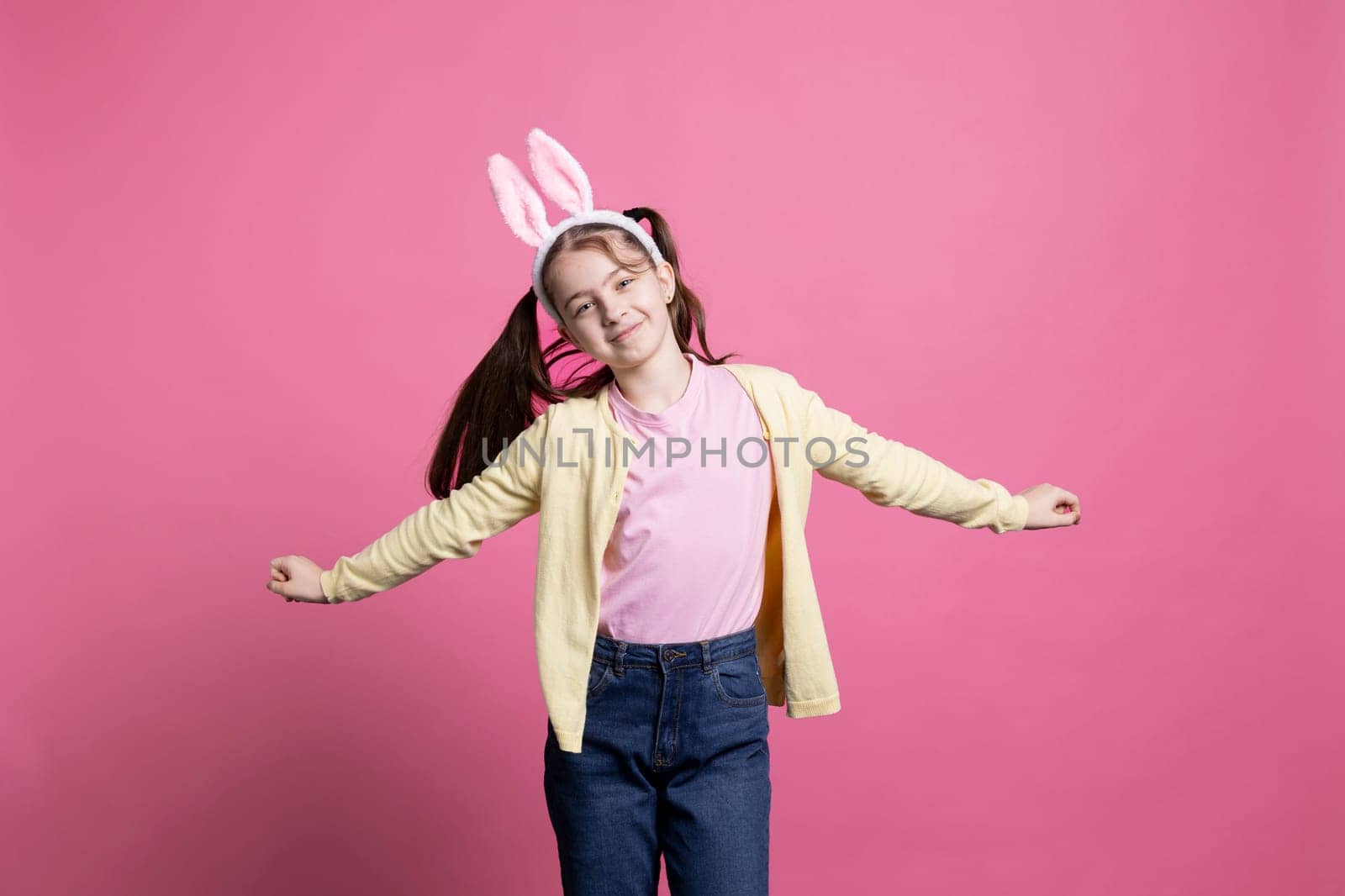 Happy schoolgirl with pigtails and bunny ears dancing in studio, showing modern lovely dance moves in front of camera. Young child celebrating easter holiday festivity, carefree junior.