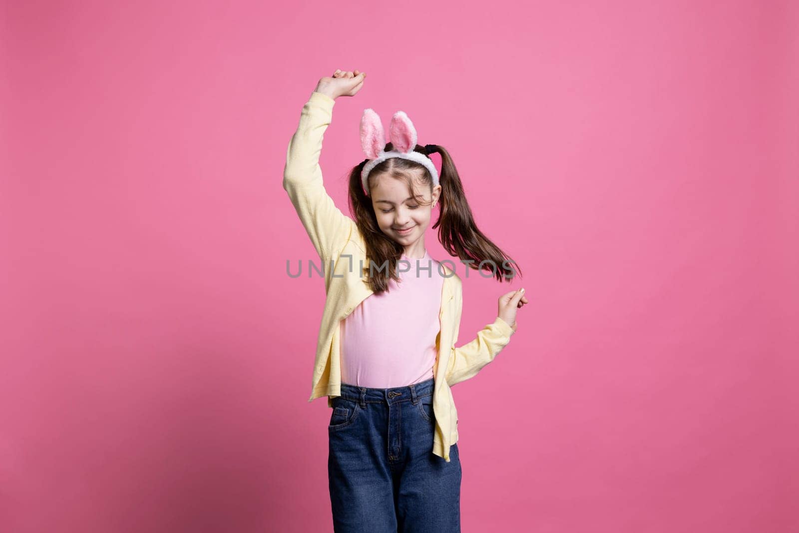 Energetic and positive kid dancing in studio while wearing bunny ears in excitement of Easter Sunday celebrations. Pleased carefree youngster who displays comfort in her dance skills.