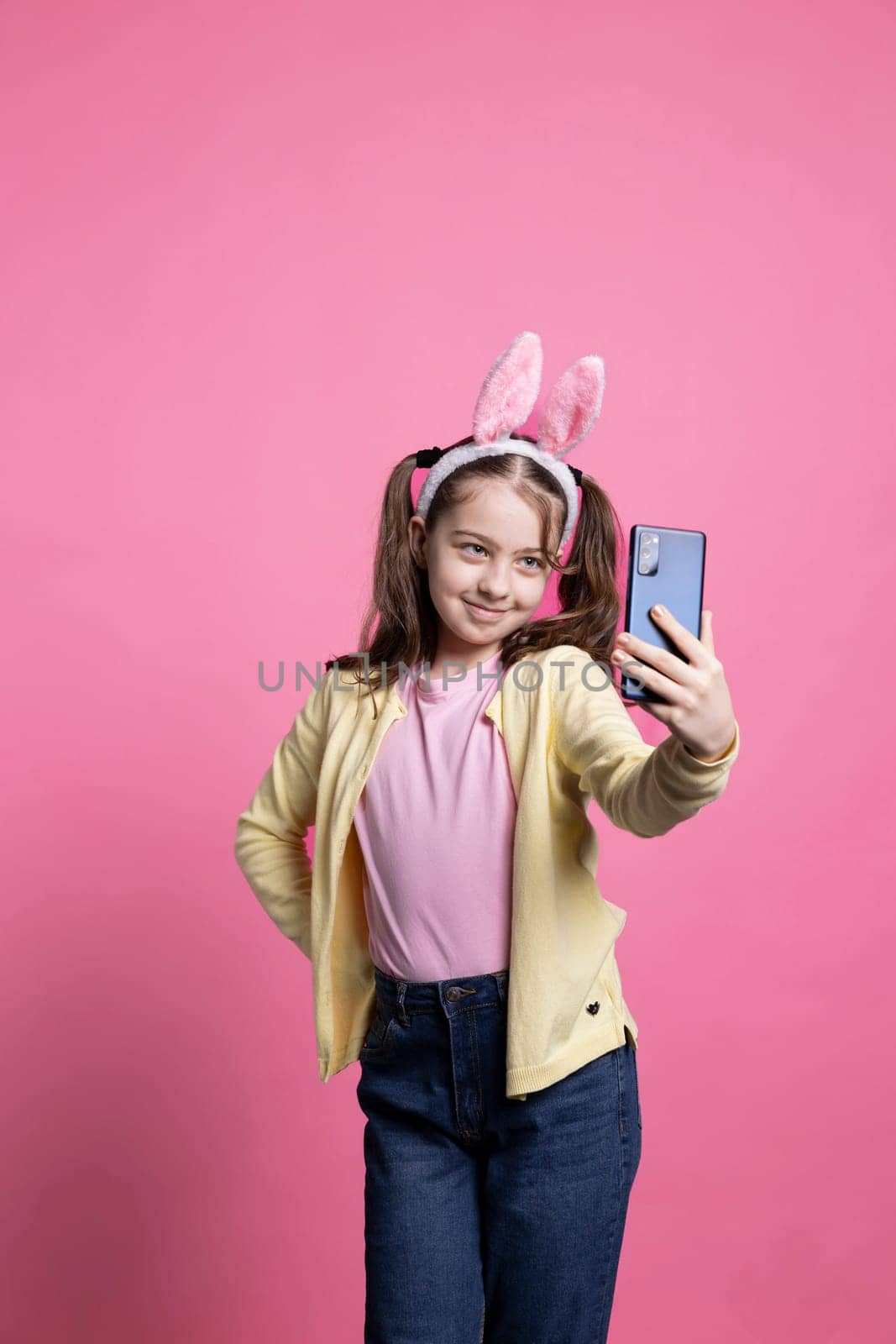 Positive cute schoolgirl taking pictures with her mobile phone in studio by DCStudio