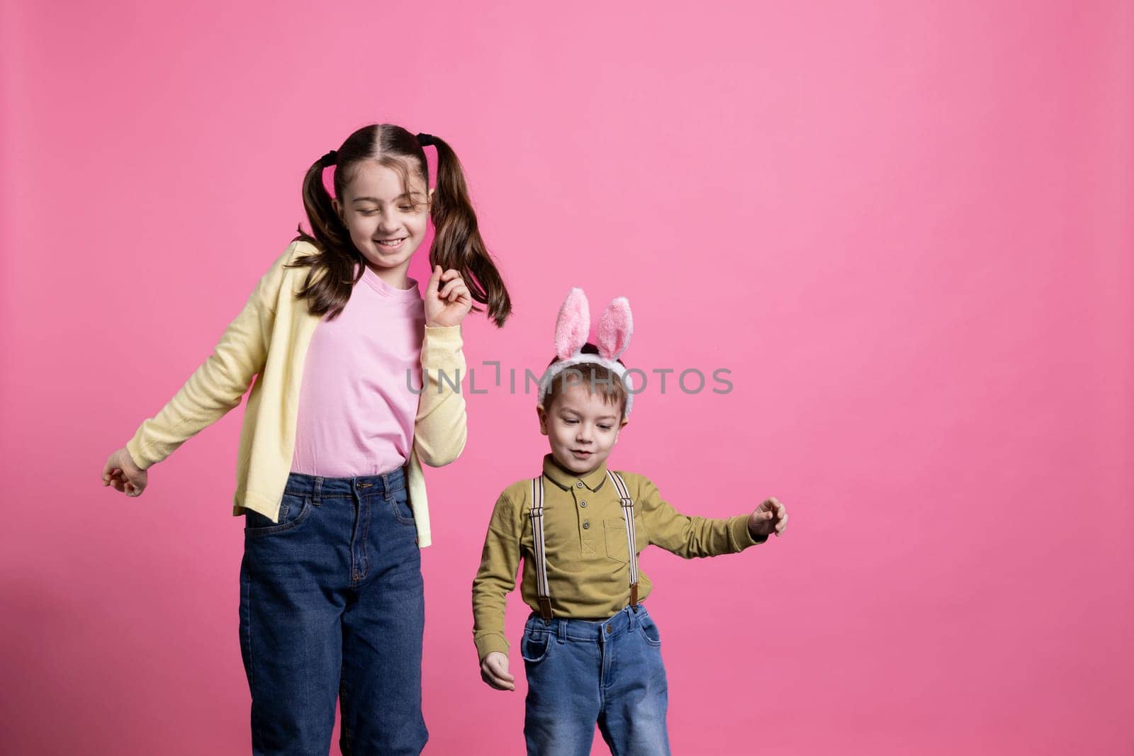 Cute young children dancing around in front of camera, feeling happy and curious about easter celebration or gifts. Brother and sister enjoying spring holiday, little boy wearing bunny ears.