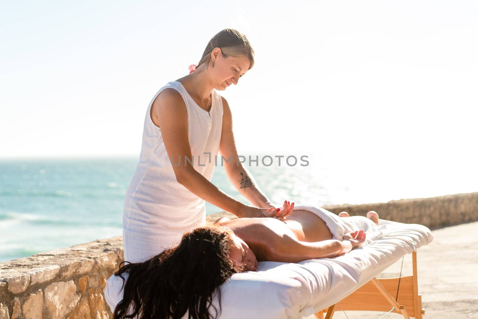 Woman enjoying hand and back massage on ocean shore by andreonegin
