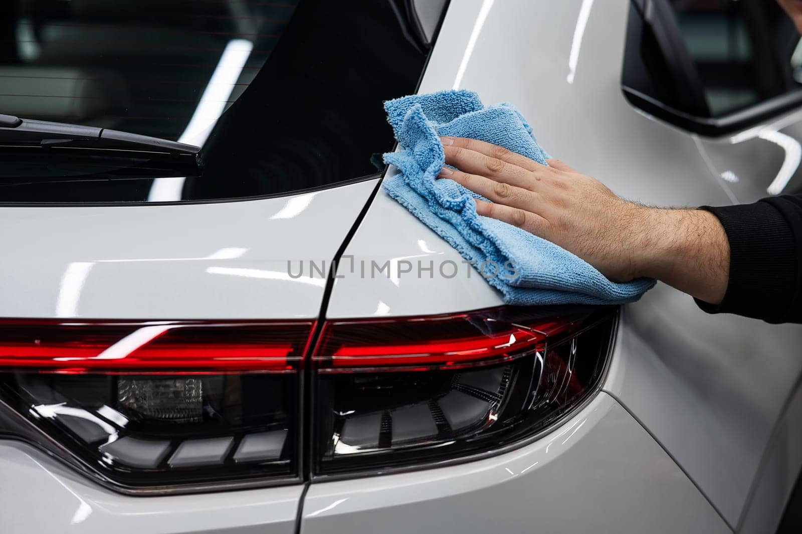 A mechanic wipes the body of a white car with a microfiber cloth. by mrwed54