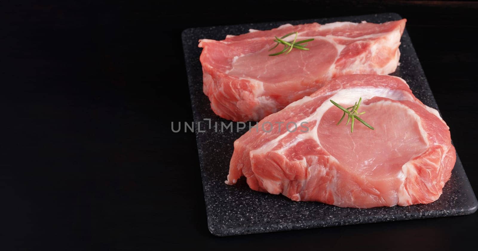 Raw pork steak with rosemary on a black table by NataliPopova