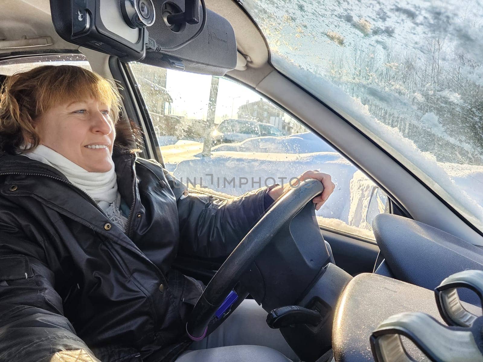 A woman in a car taking a selfie while enjoying a drive. Female driver in warm jacket posing inside car in warm jacket on cold day by keleny