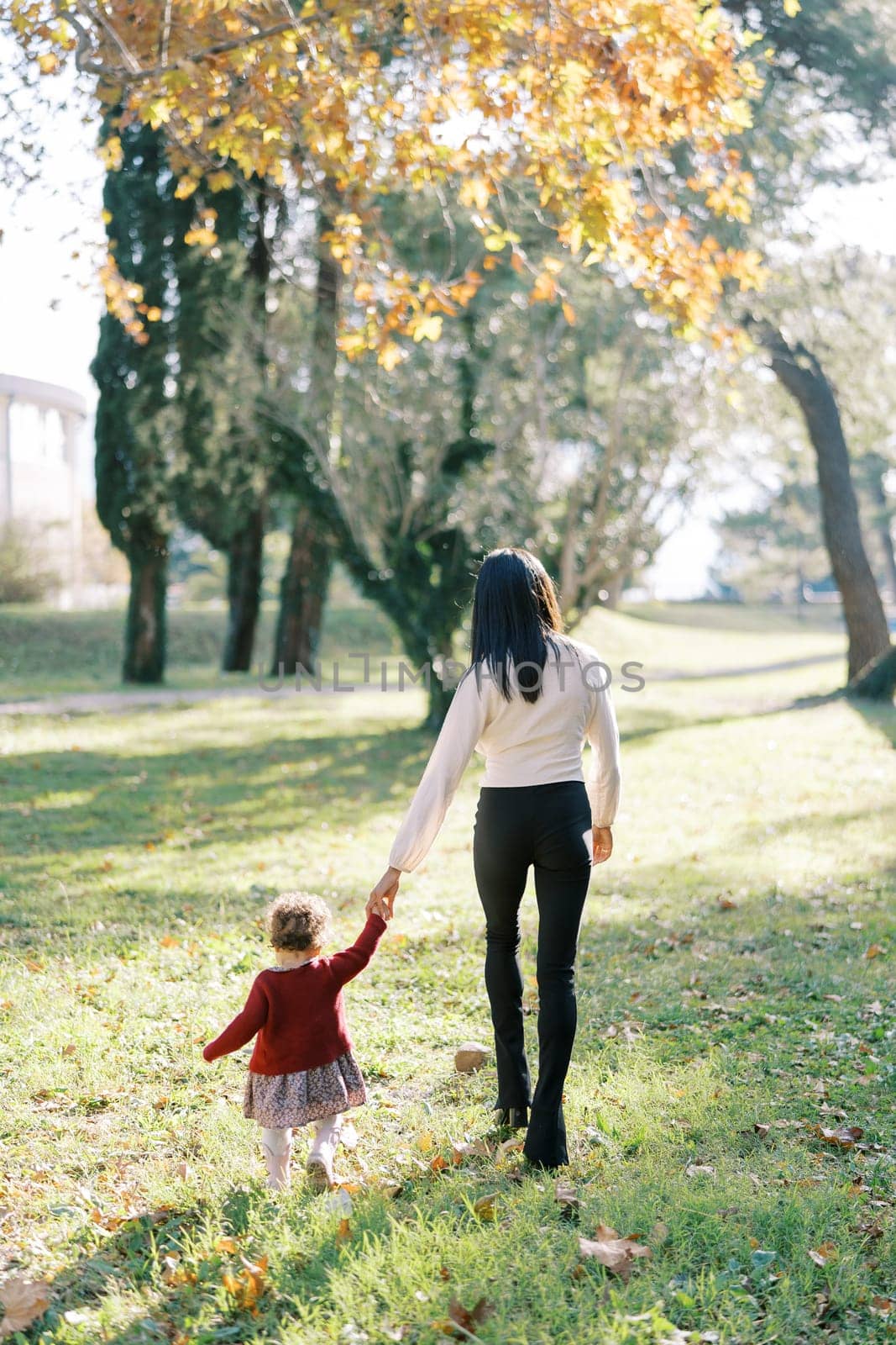 Little girl walks with her mom holding hands in the park. High quality photo