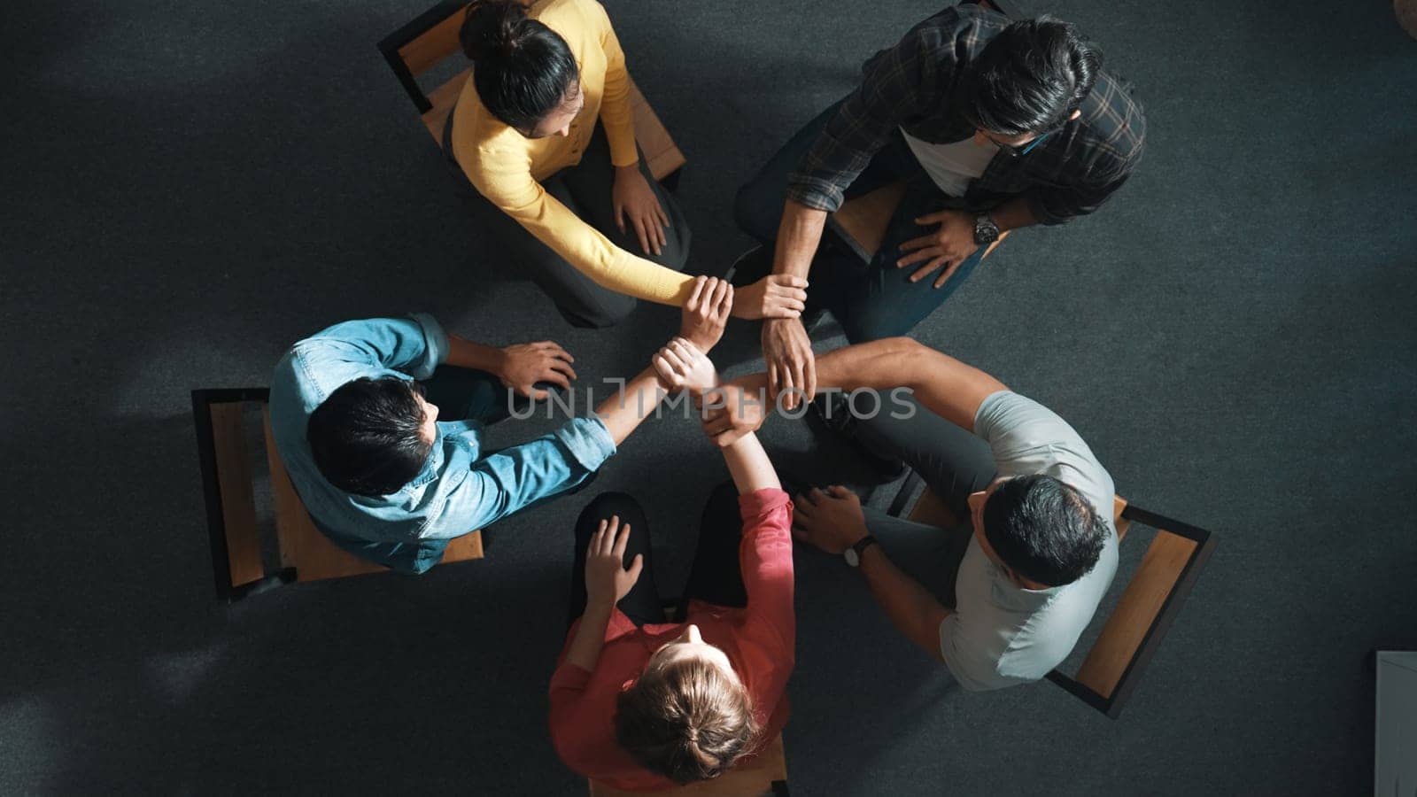 Top down aerial view of diverse business people hold wrist while sitting circle together. Faithful prayers holding wrist or hand of each other. Represented teamwork, unity, togetherness. Symposium.