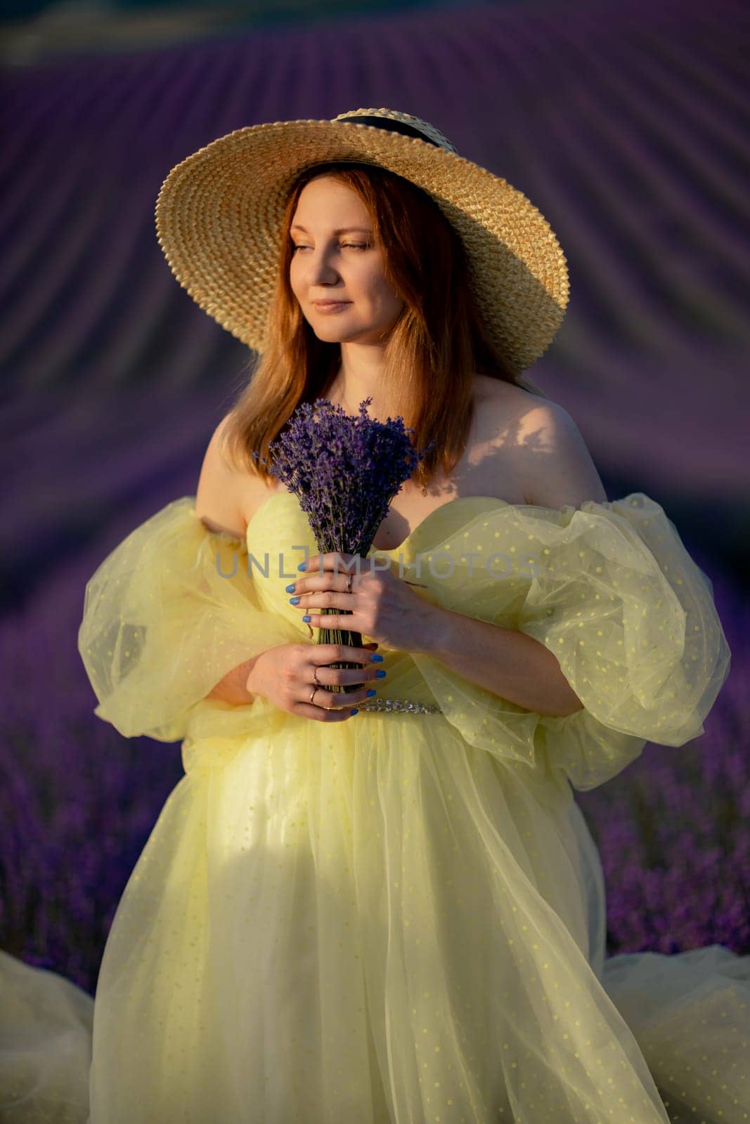 Lavender sunset girl. A laughing girl in a blue dress with flowing hair in a hat walks through a lilac field, holds a bouquet of lavender in her hands. Aromatherapy concept, lavender oil, photo session in lavender.