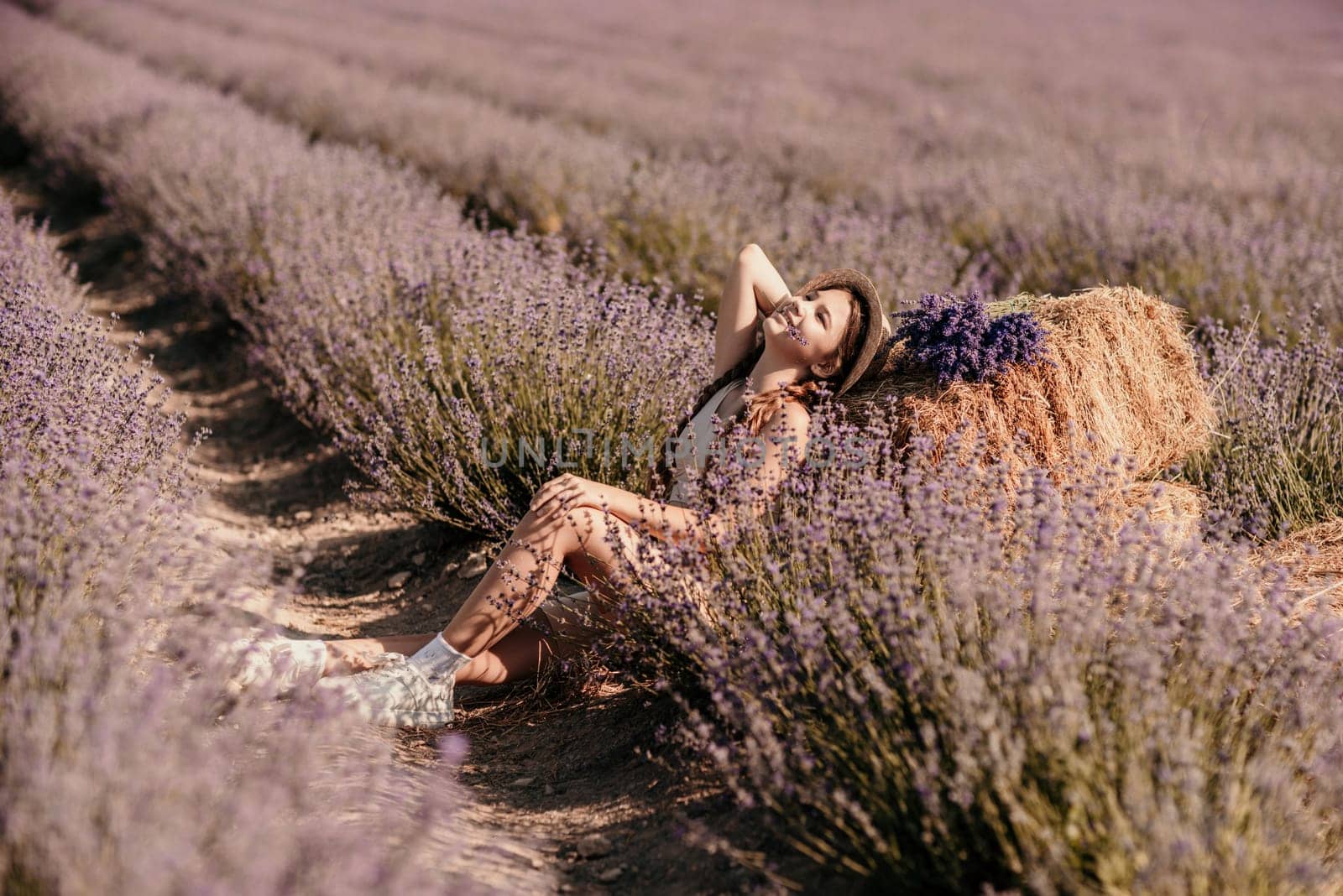 A young girl is sitting in a field of purple flowers, holding a purple flower in her hand. She is smiling and she is enjoying the moment. Concept of happiness and contentment