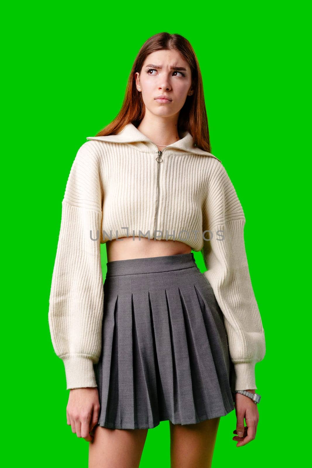 A woman wearing a skirt and sweater stands confidently against a vibrant green background. Her posture exudes strength and poise as she gazes ahead.
