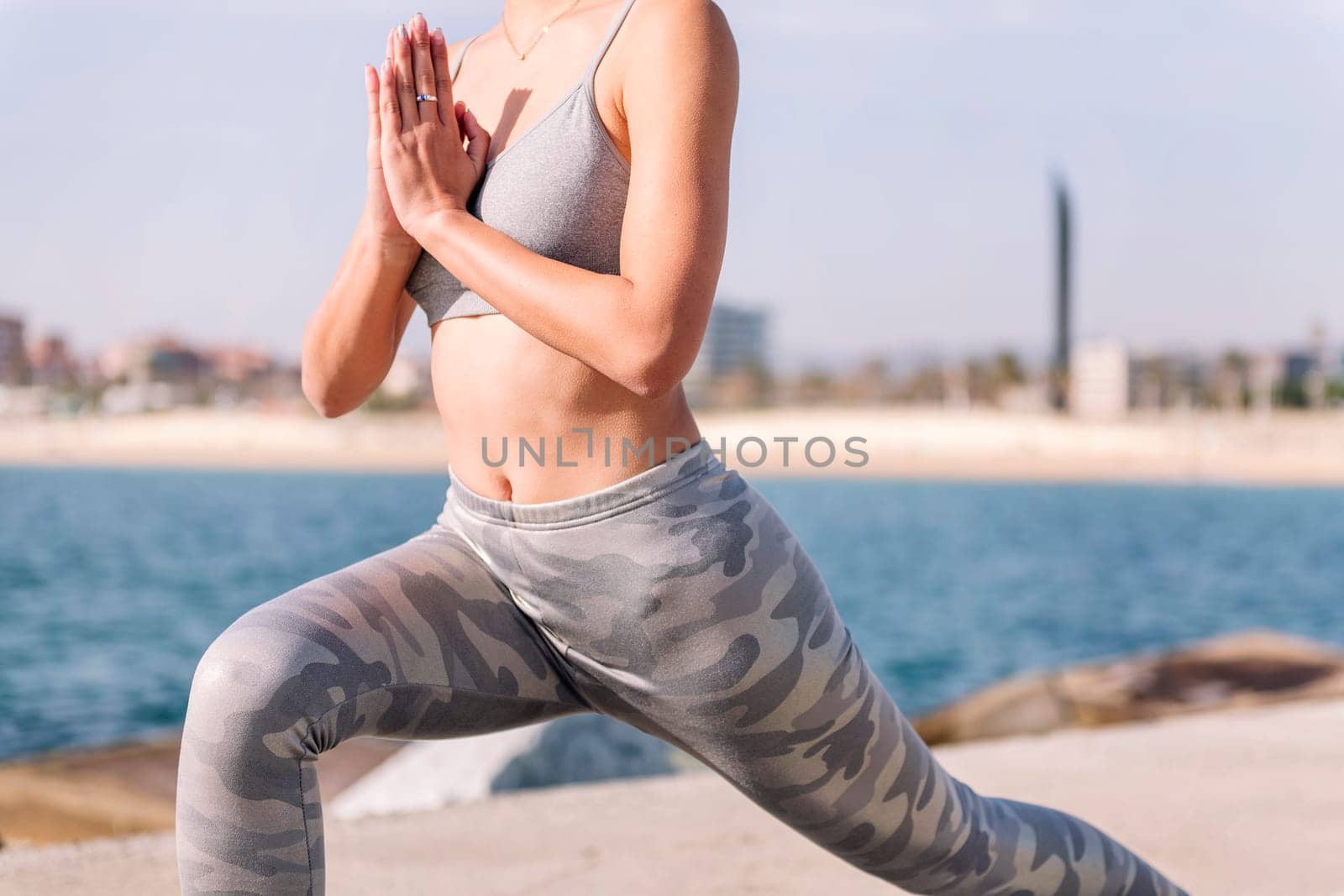 cutout of torso of unrecognizable woman in sportswear practicing yoga by the sea, relaxation and healthy lifestyle concept