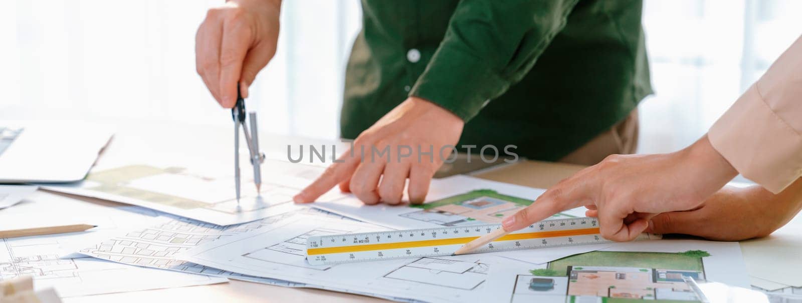 A cropped image of professional engineer using divider to measure blueprint at meeting table with blueprint, laptop and architectural equipment scatter around. Closeup. Delineation.