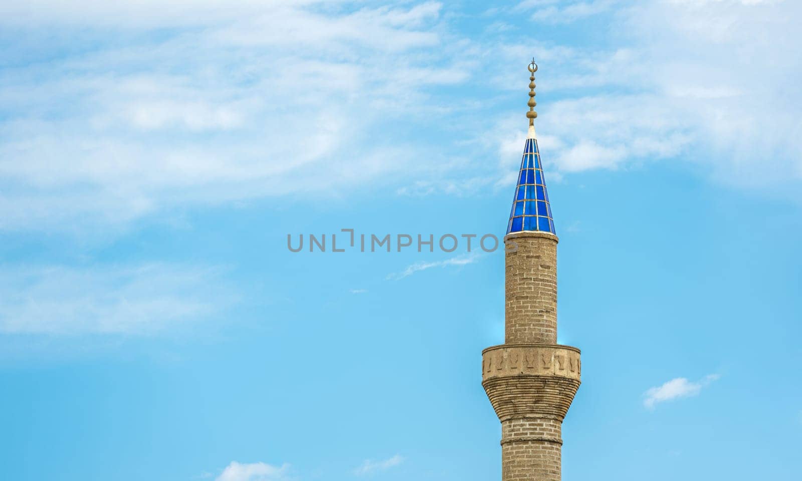 Mosque minaret with blue glass in front of a sunny, cloudless blue sky