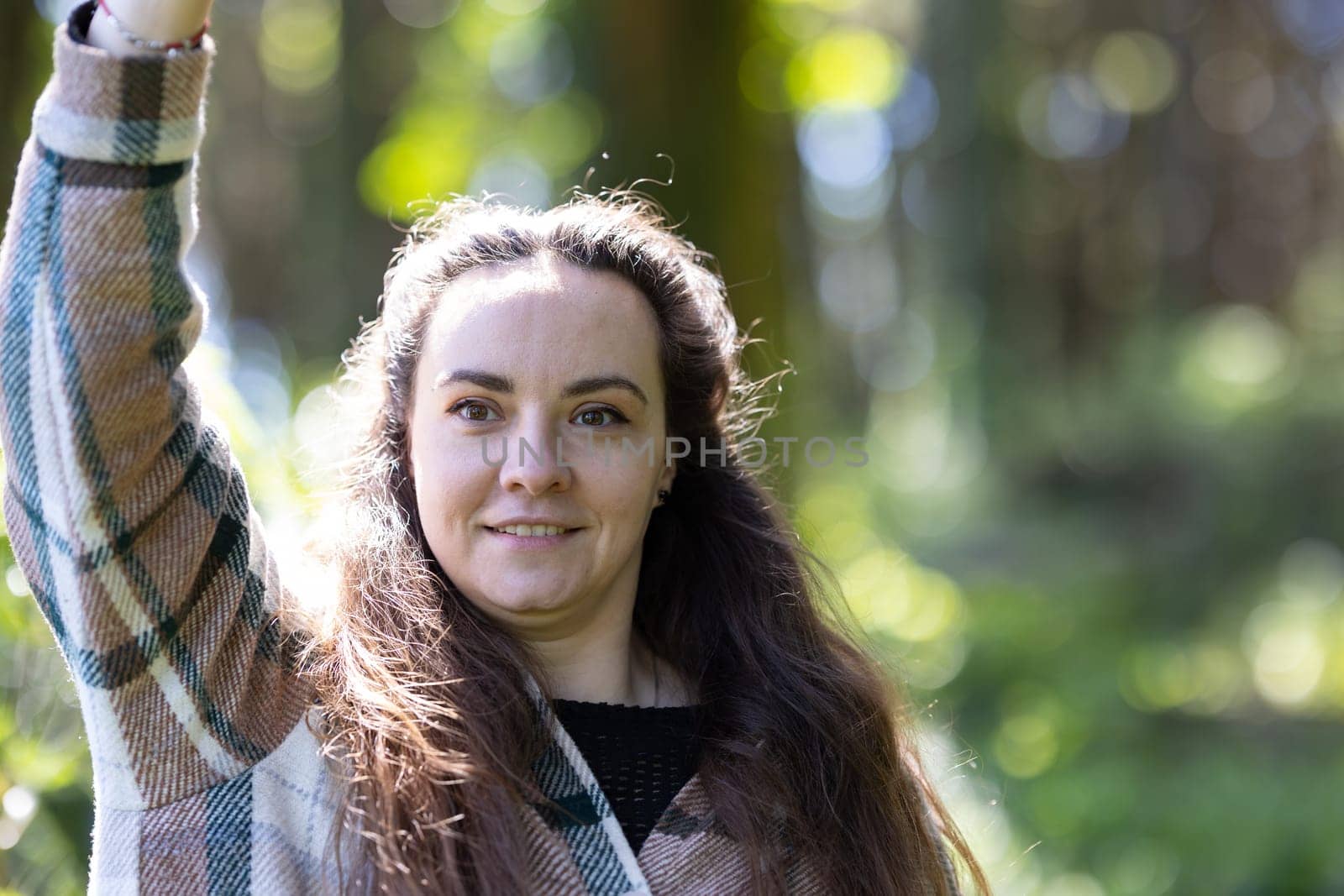 A woman with long brown hair is standing outdoors with friends, wearing a stylish plaid jacket. She exudes confidence and style as she interacts with her companions.