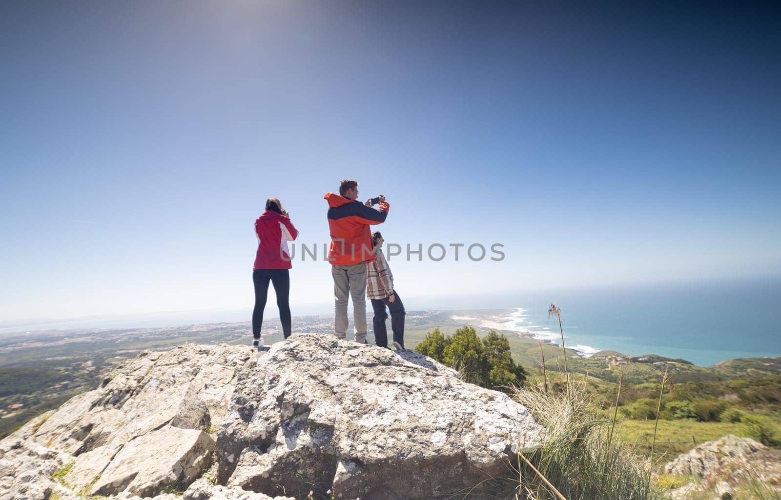 Three People Standing on Top of a Mountain Overlooking the Ocean by Studia72